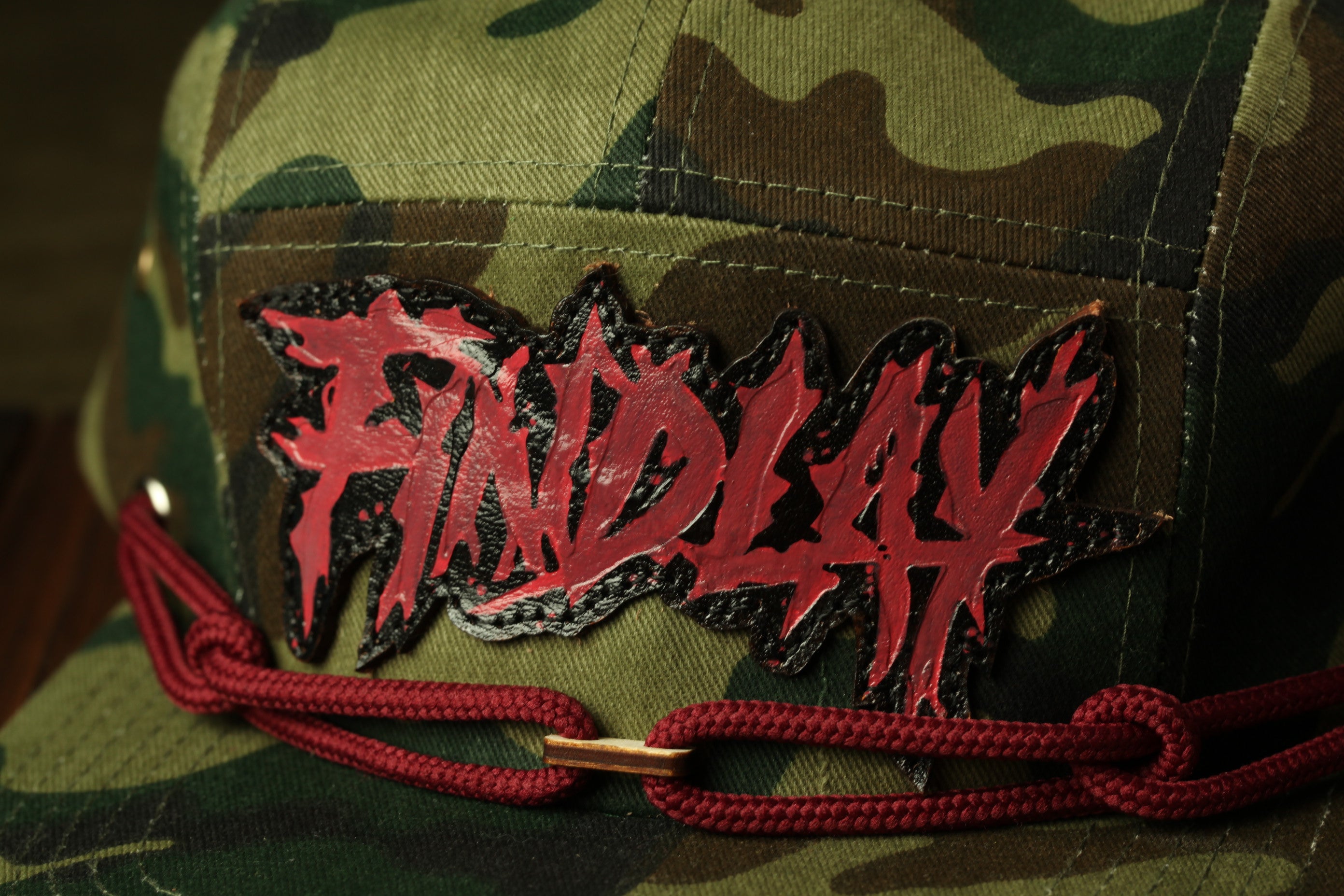 A close-up of a camouflage-patterned hat with a red and black graphic patch that says "FINDlay" on it.