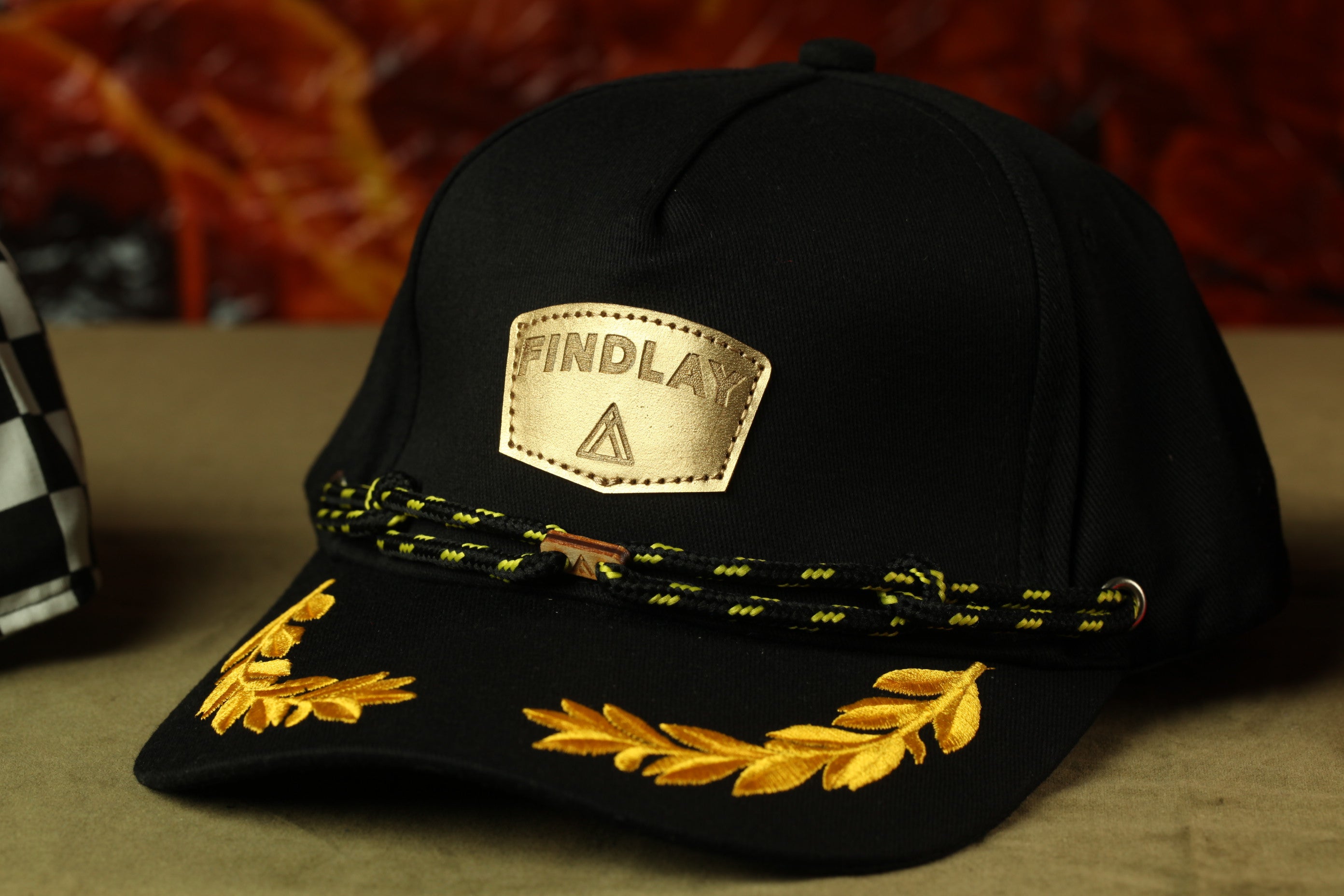 A black baseball cap with gold embroidered leaves and a gold-colored patch on the front, which says "FINDLAY".