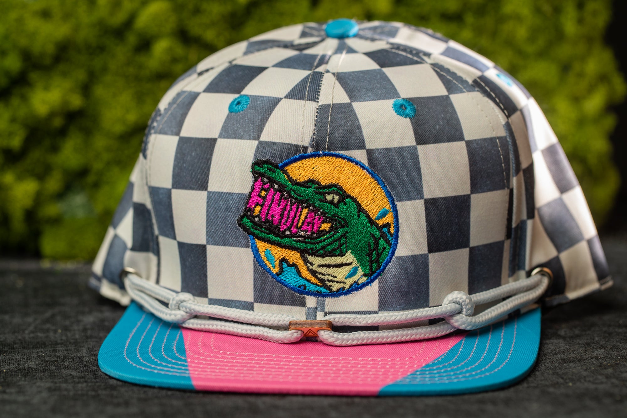 A colorful baseball cap with a checkered pattern and a graphic of a green alligator on the front.