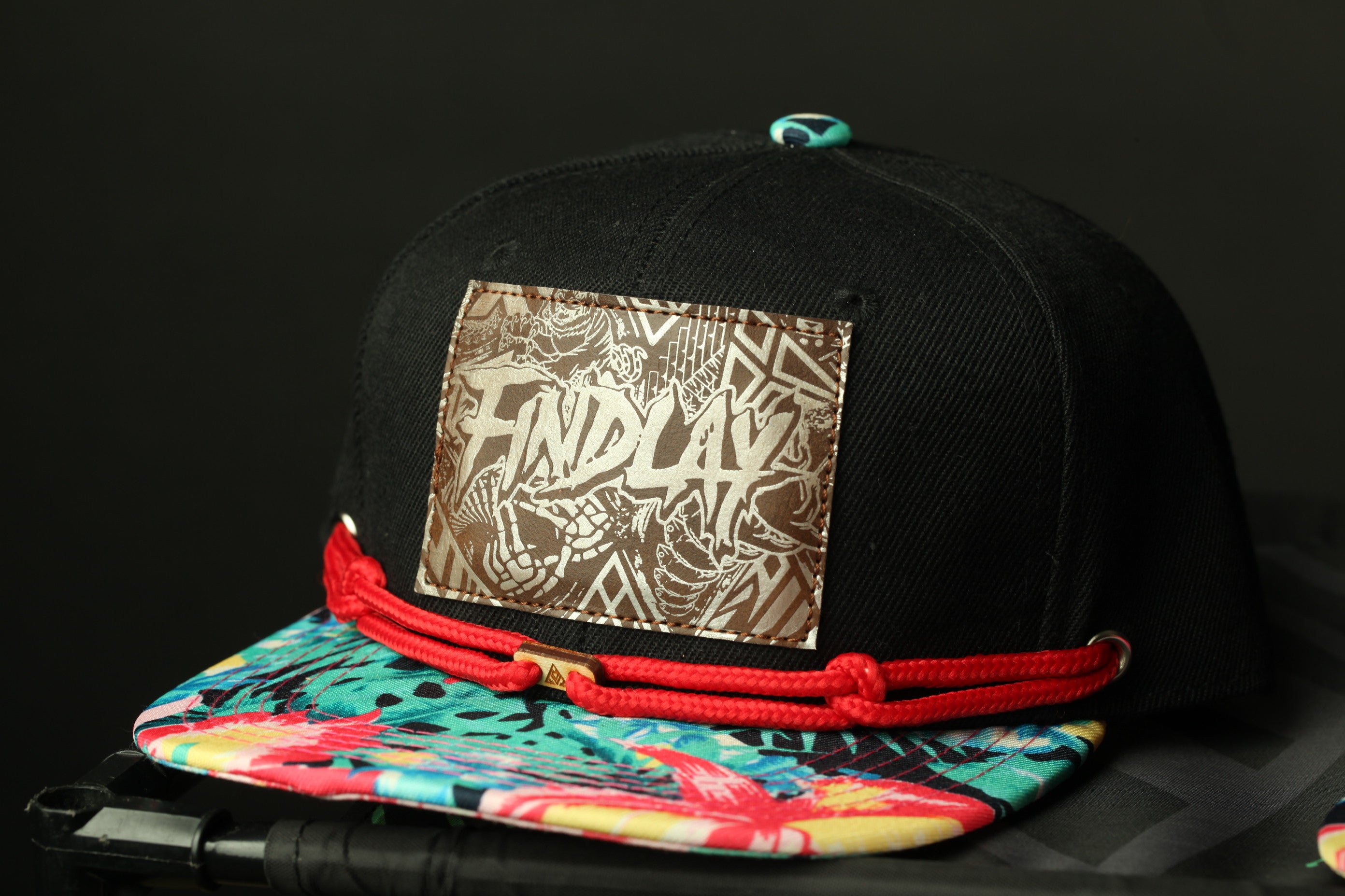 A black baseball cap with a colorful floral pattern and a patch on the front displaying the text "FIND LAY".