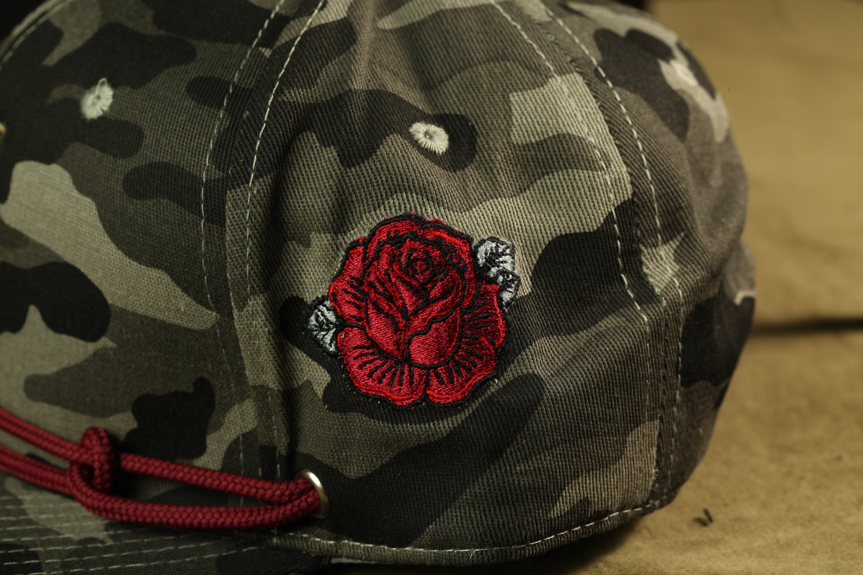 A close-up view of a camouflage baseball cap with a red rose embroidered on the front.