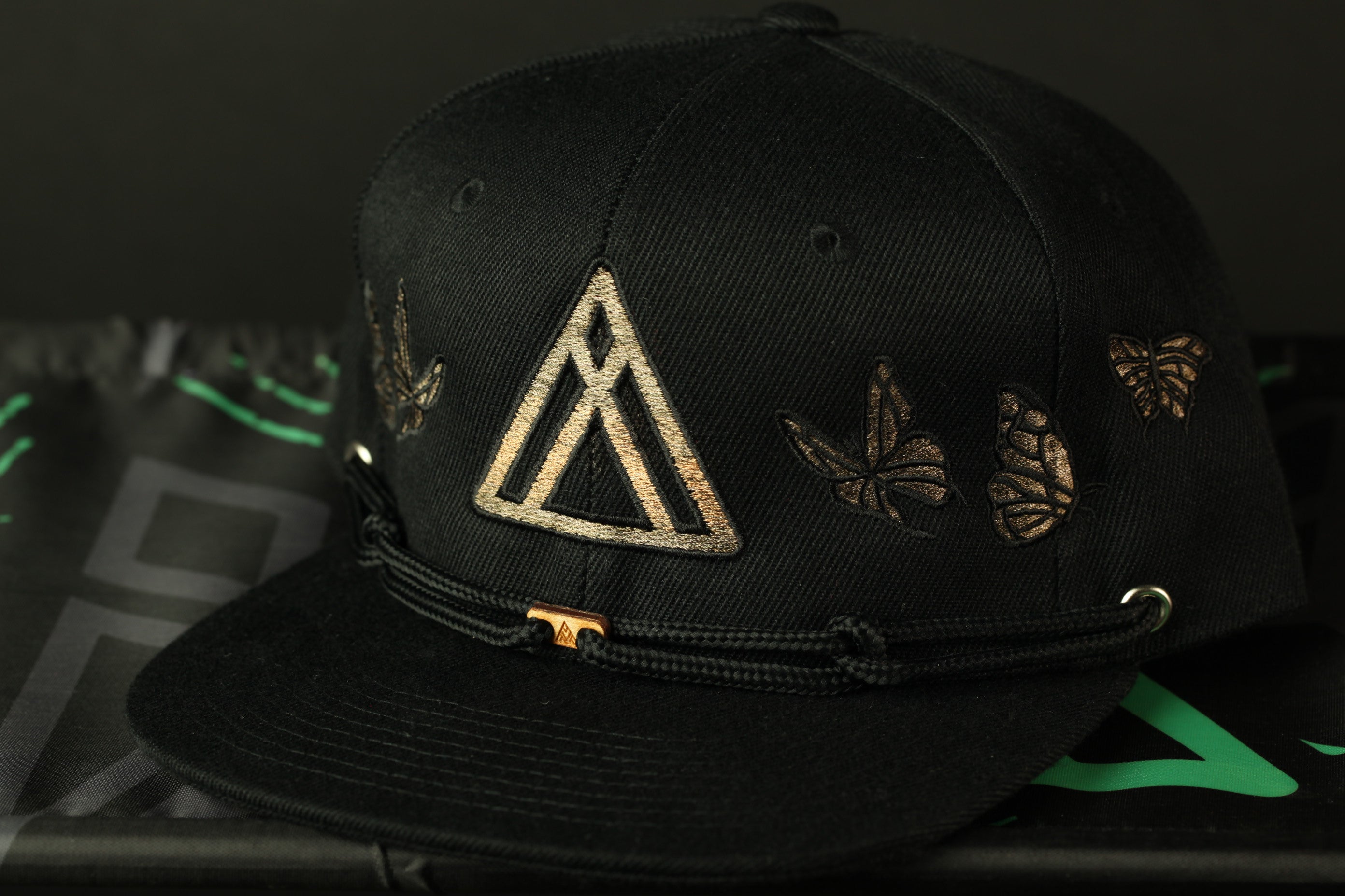 A black baseball cap with a gold triangle design and butterflies on the brim.