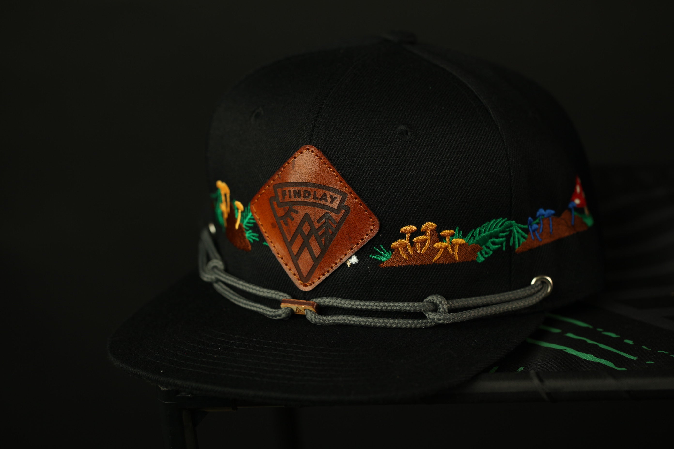 A black baseball cap with a leather patch and colorful embroidered designs on the brim.