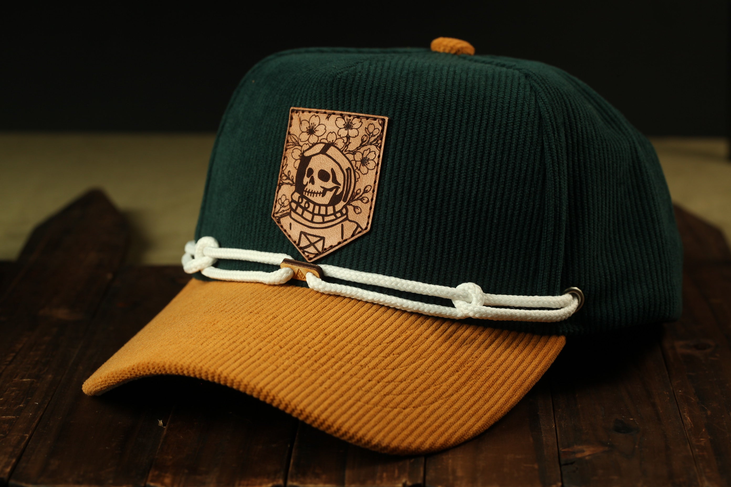 A green baseball cap with a skull and floral design on the front, resting on a wooden surface.