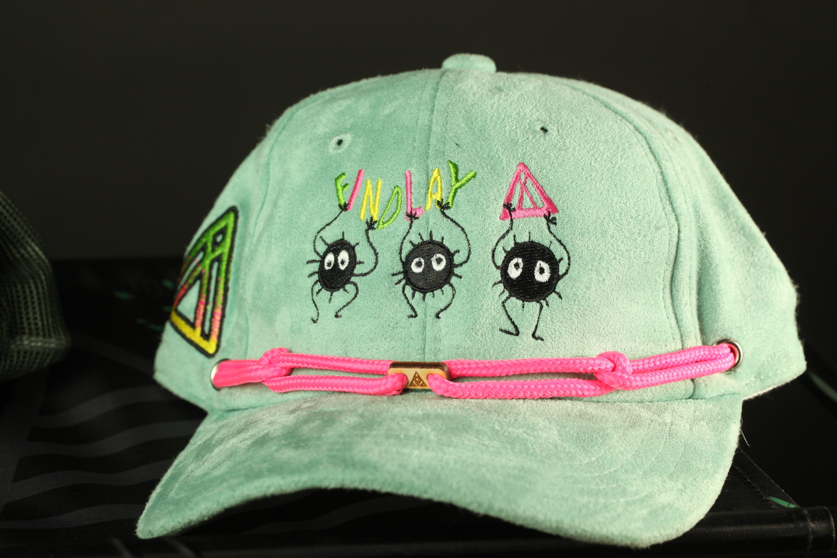 A light green baseball cap with a pink braided strap and three cartoon spider characters printed on it.