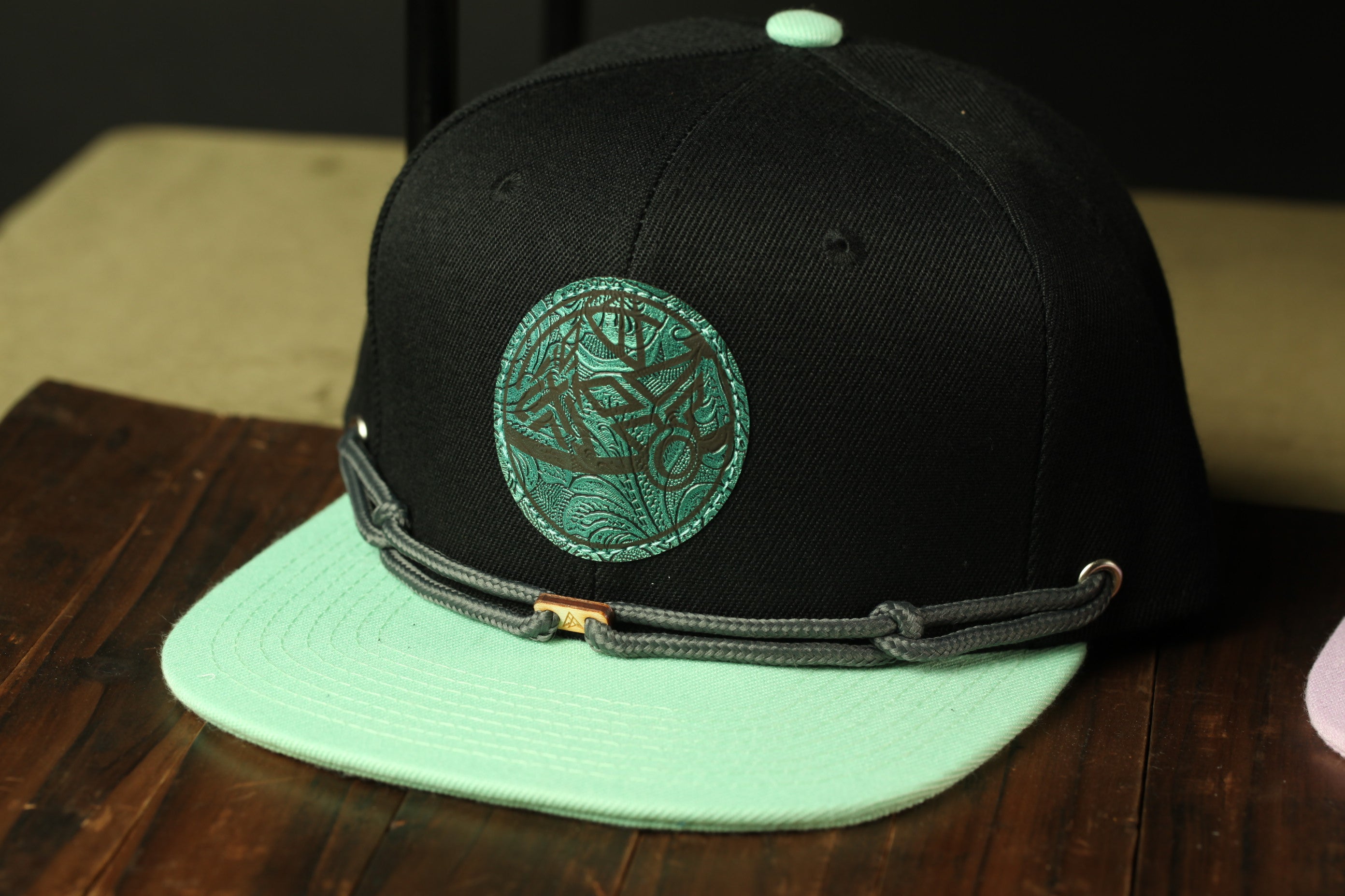 A black baseball cap with a green and teal patterned logo, placed on a wooden surface.