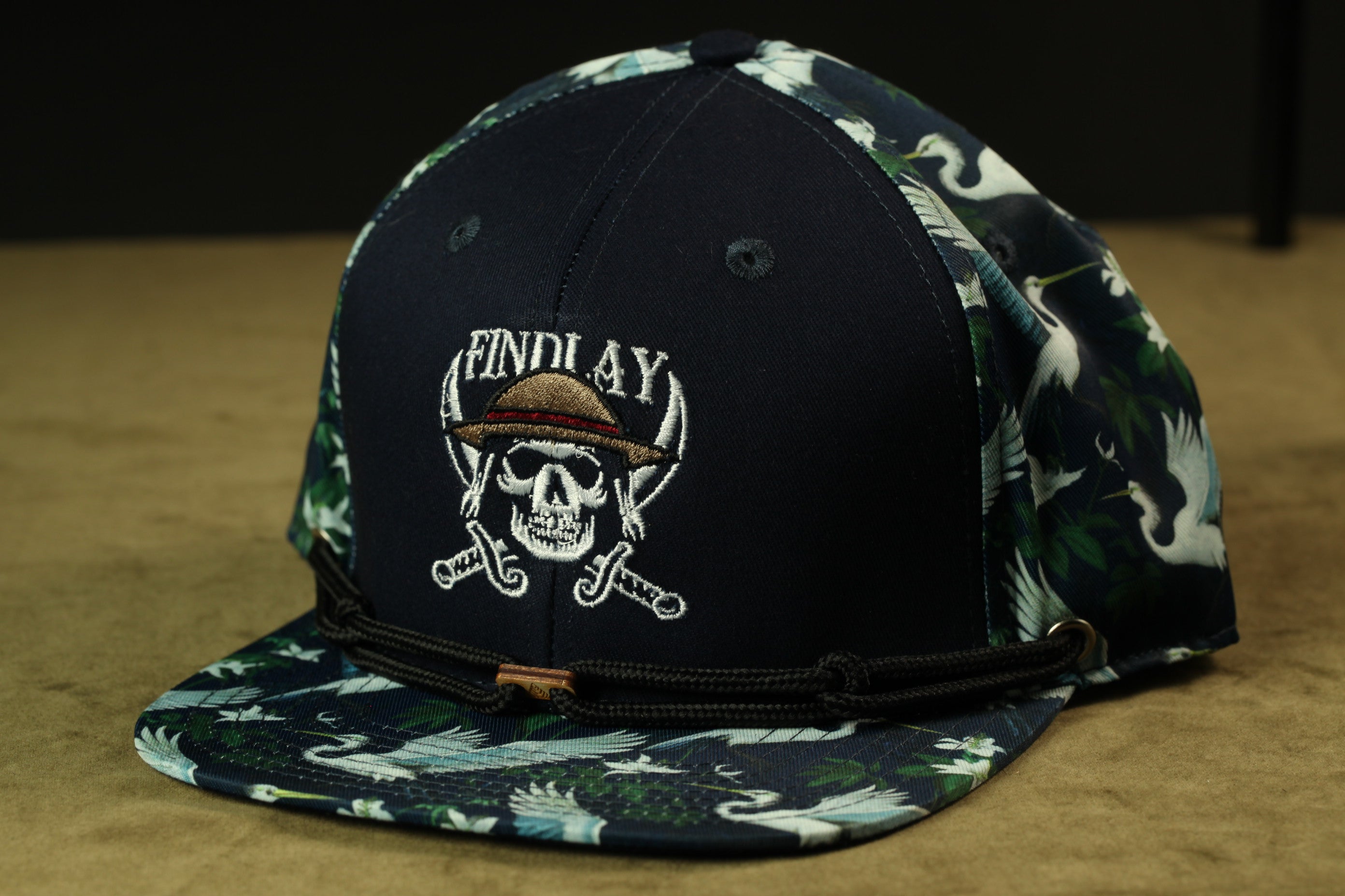 A navy blue baseball cap with a skull and crossbones design, featuring the text "FINDlay" on the front.