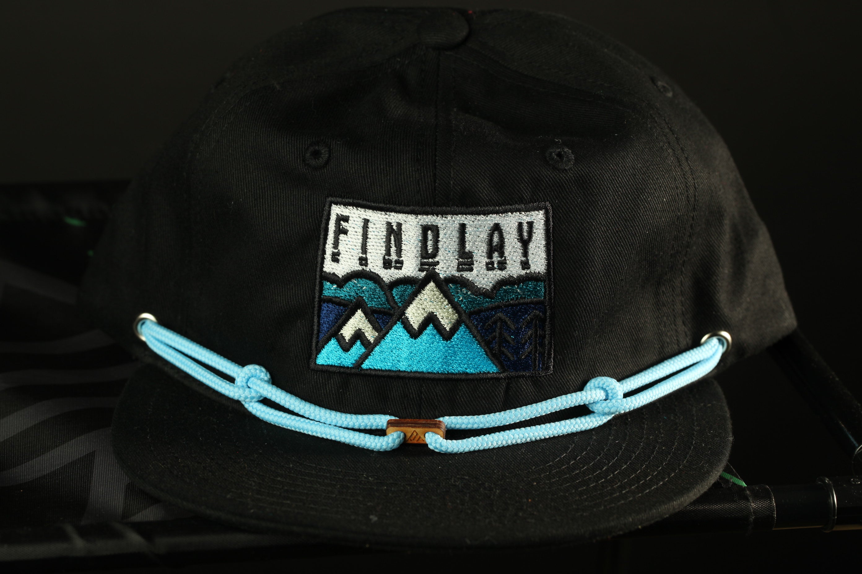 A black baseball cap with a blue string and a patch on the front that says "FINDLAY".