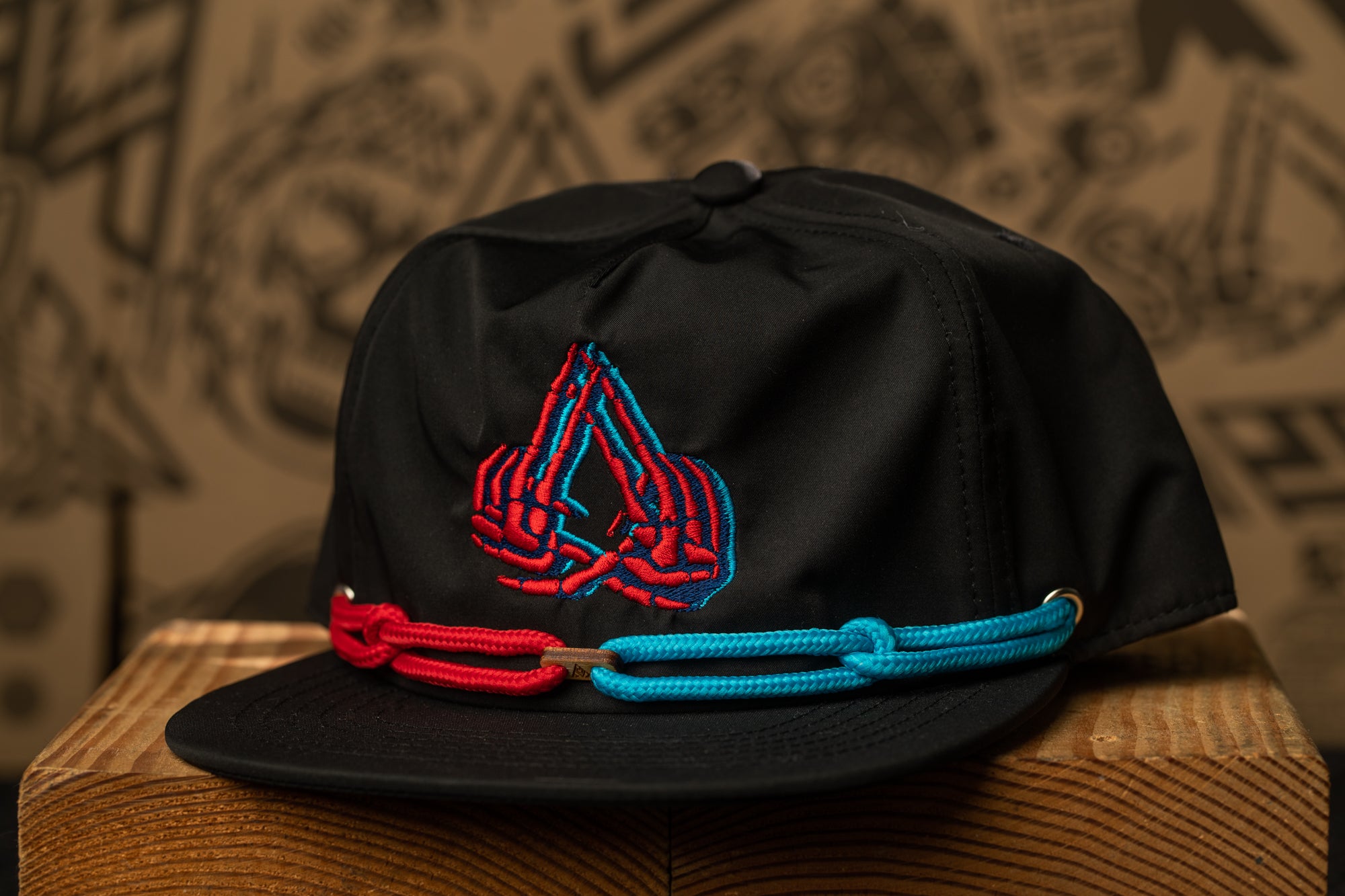A black baseball cap with a red and blue embroidered logo on the front, sitting on a wooden surface.