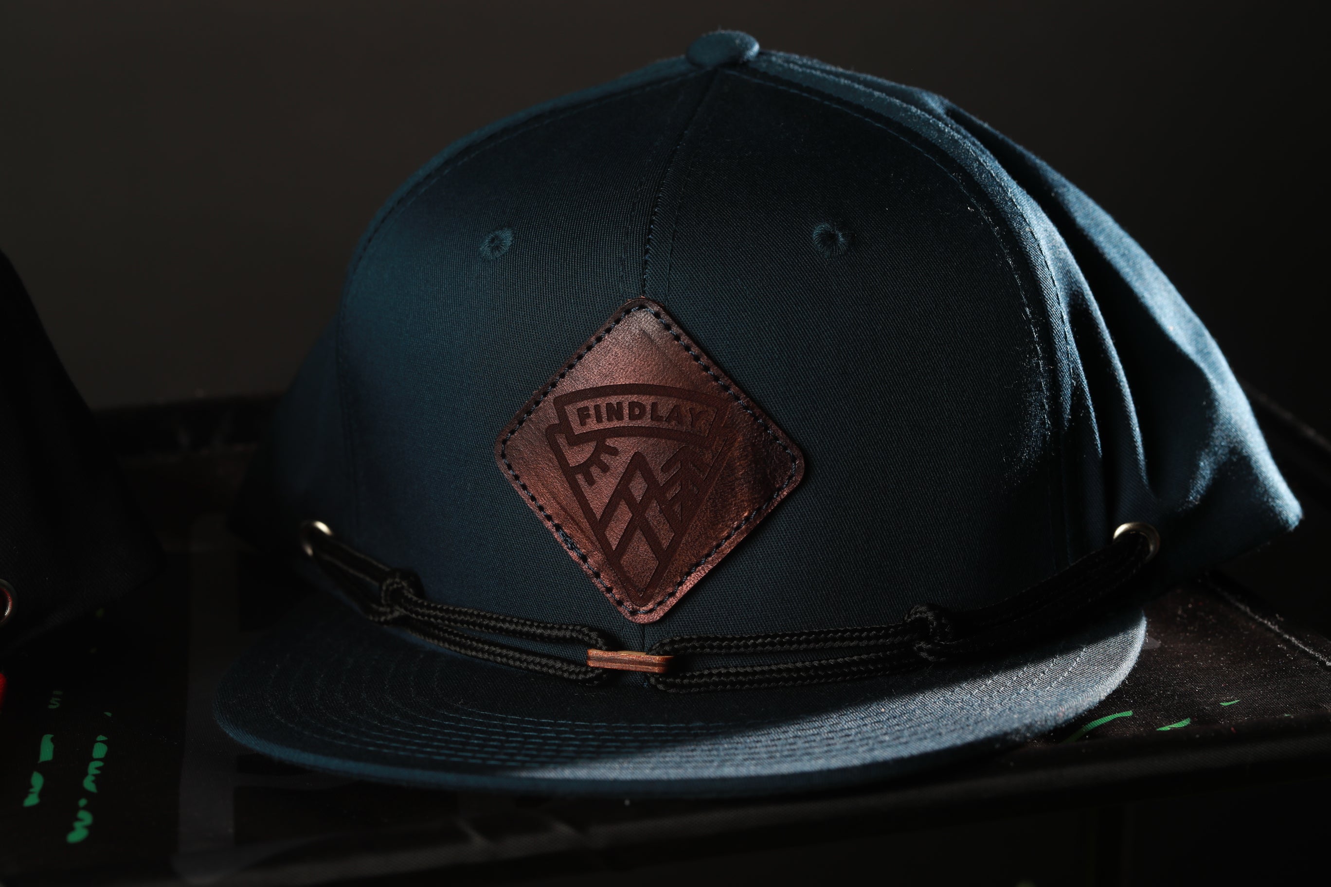 A dark blue baseball cap with a leather patch on the front, featuring a logo.