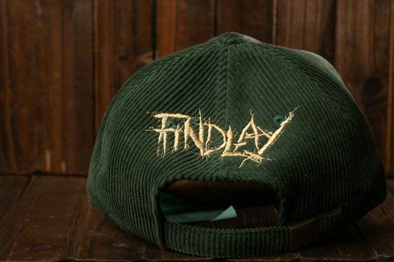 A green baseball cap with the word "FINDlay" embroidered on it, sitting on a wooden surface.