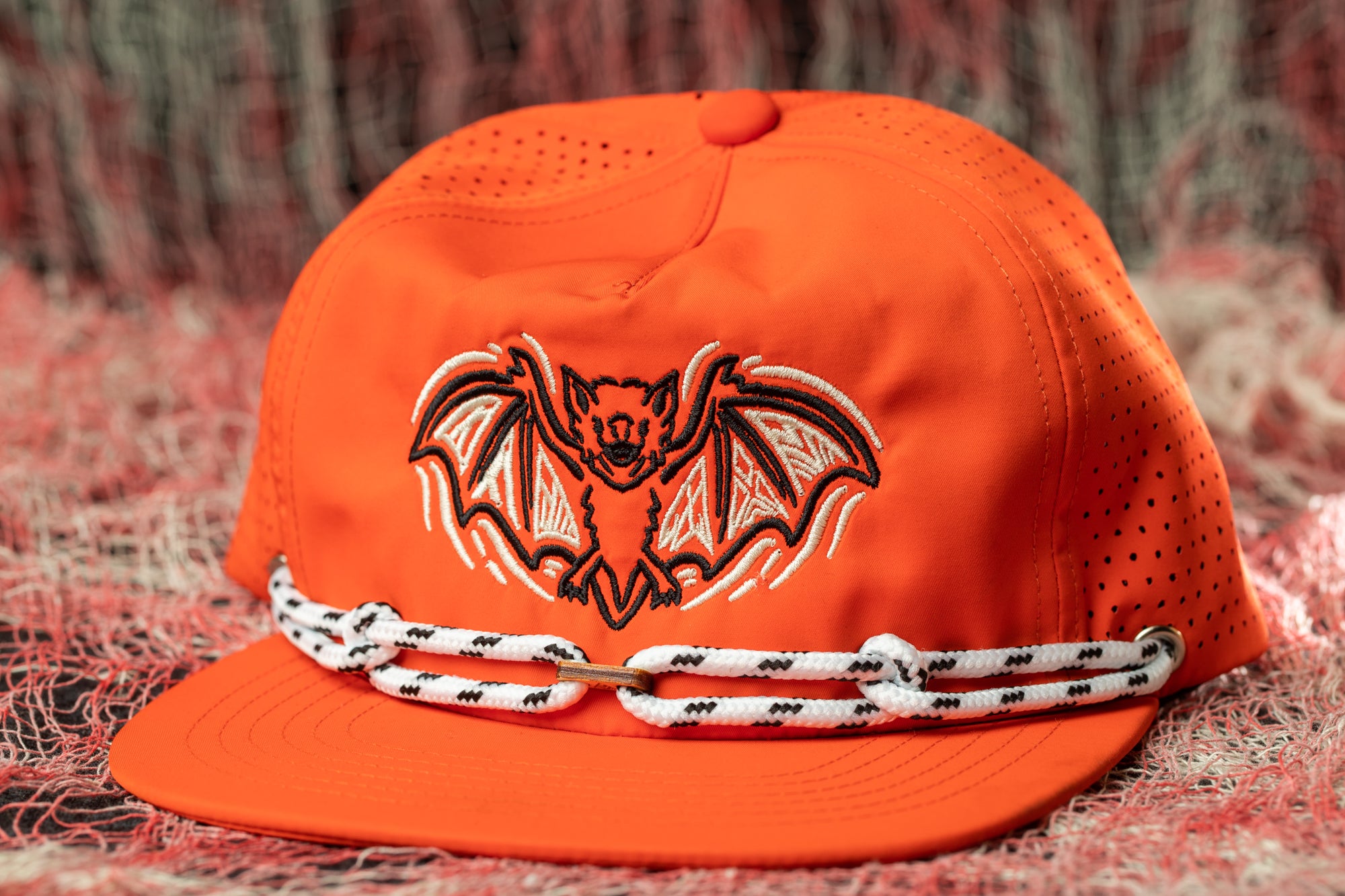 An orange baseball cap with a bat design on it, sitting on a red and white background.