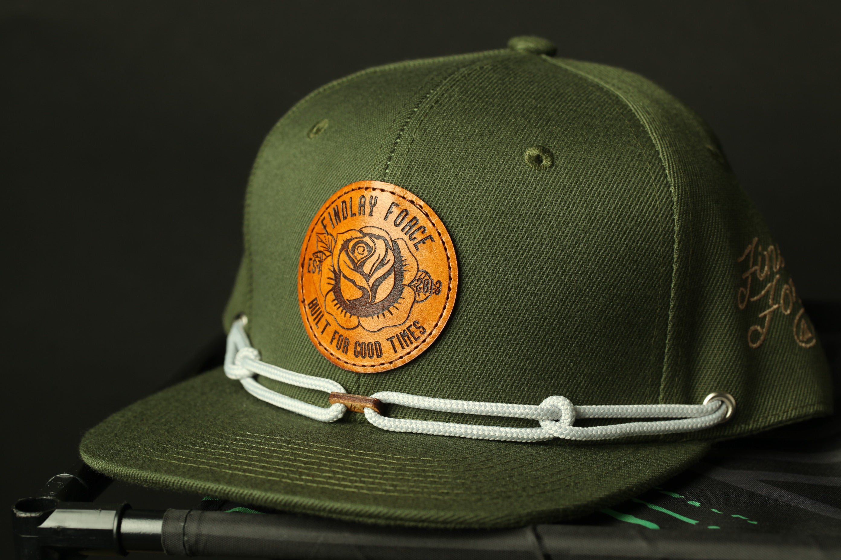 A green baseball cap with a circular patch featuring a rose and the text "FINDlay Force" and "Witch for good things" printed on it.