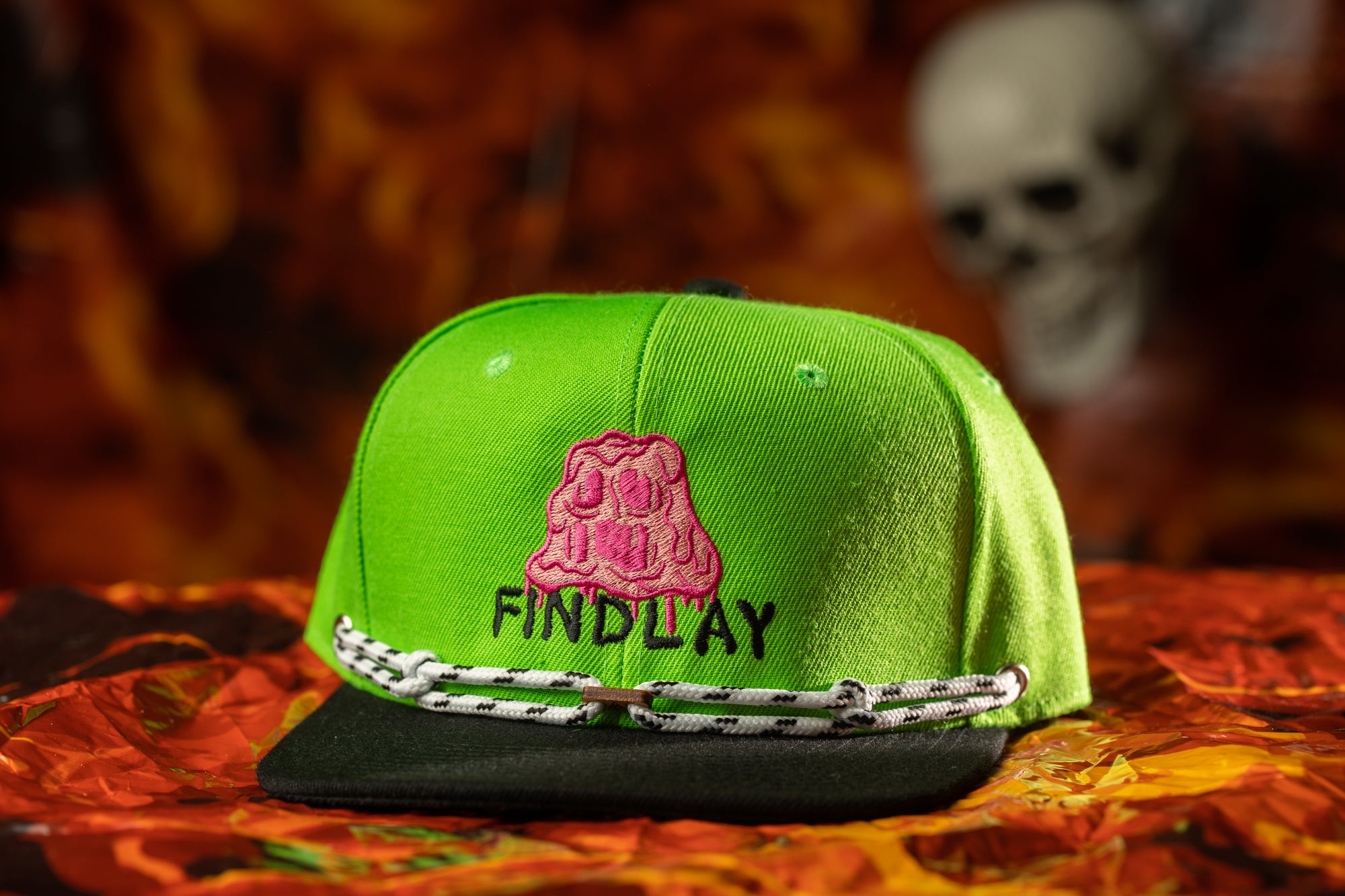 A bright green baseball cap with the text "FIND LAY" printed on it, placed on a red and orange patterned surface.