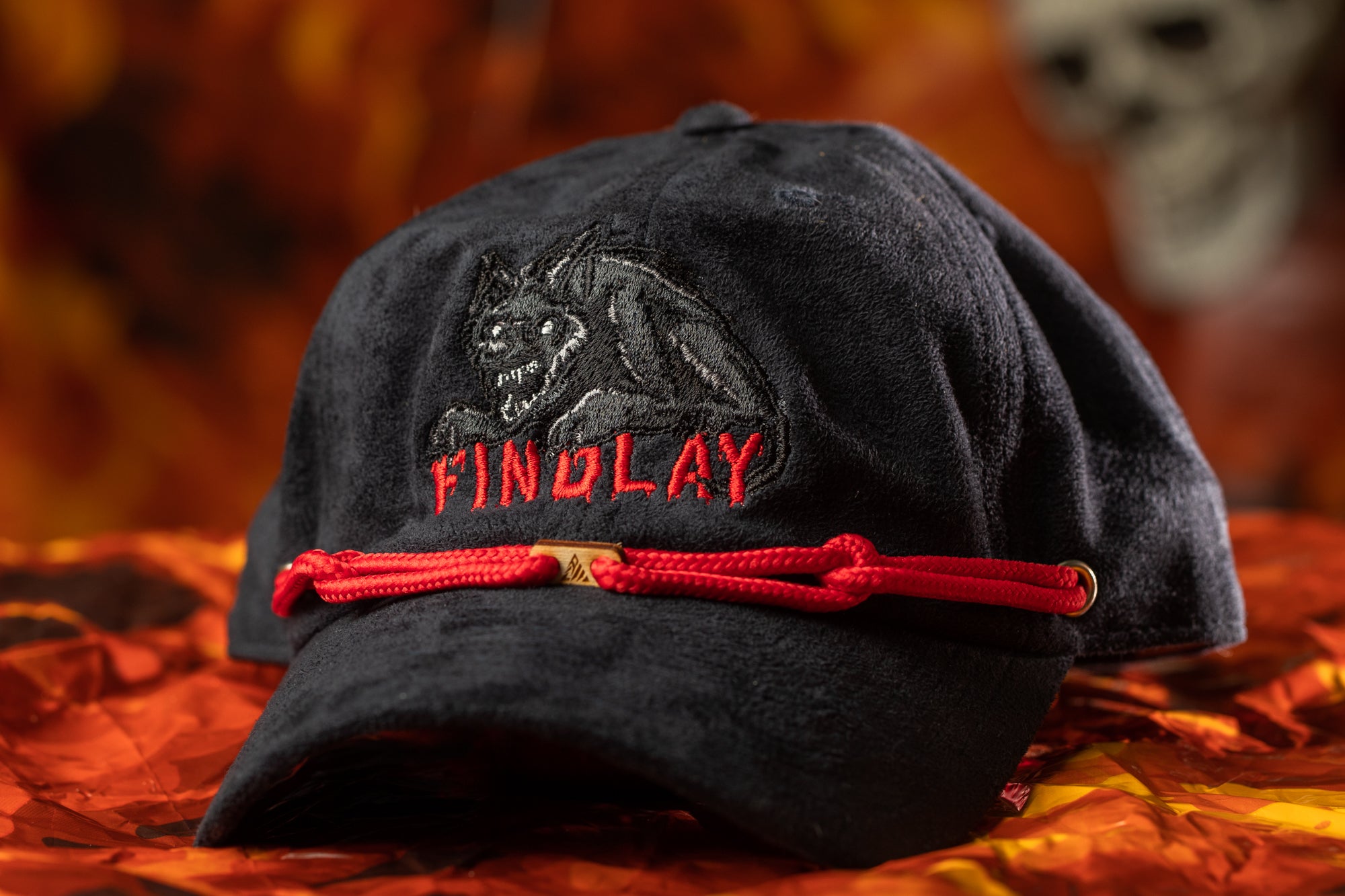 A black baseball cap with a red string and a logo on it, placed on a red and orange background.
