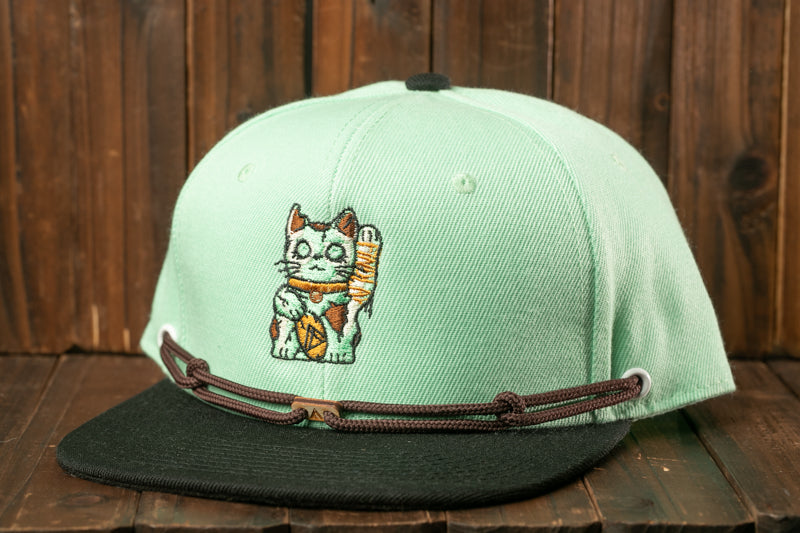 A green baseball cap with a cat embroidered on it, sitting on a wooden surface.