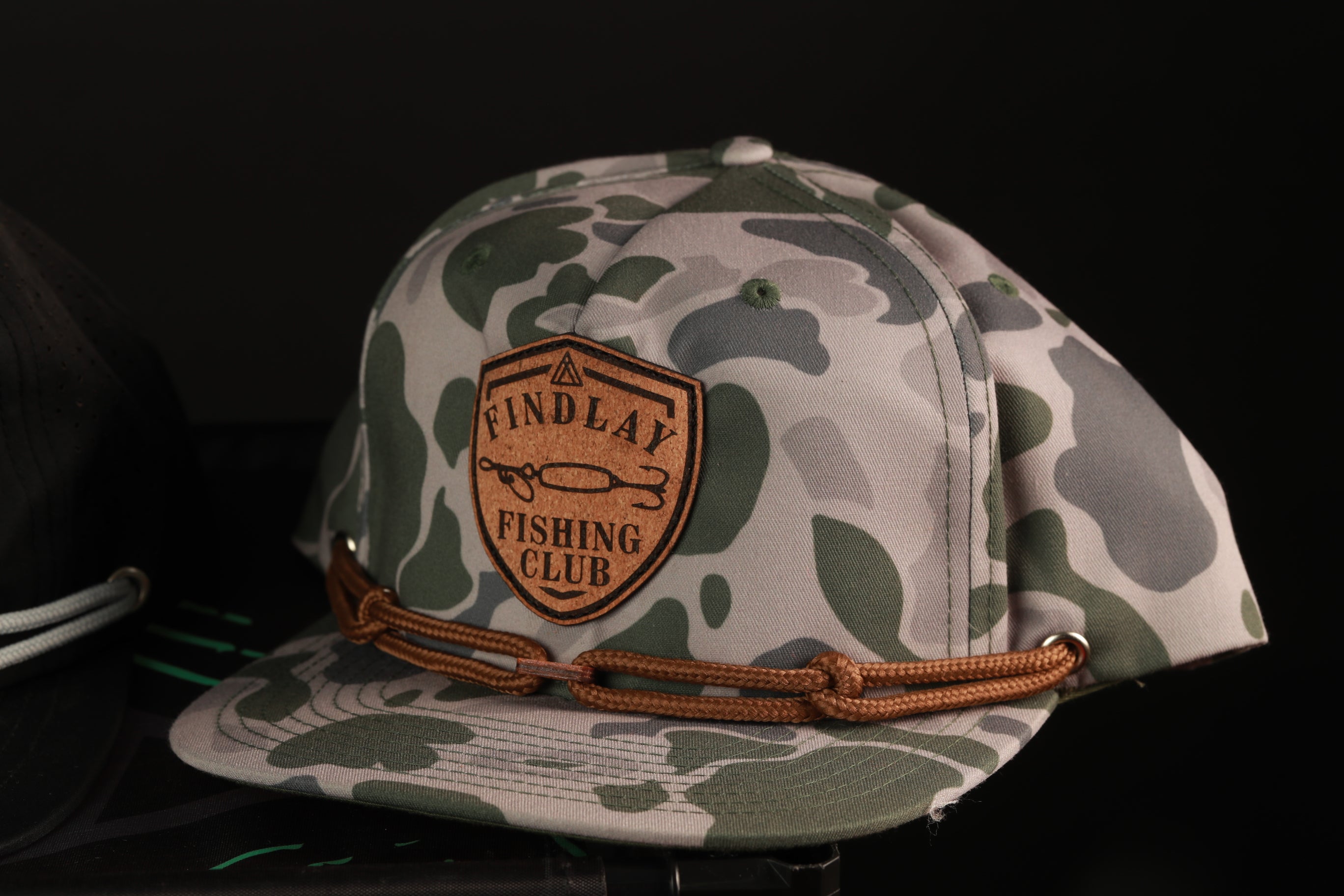 A camouflage baseball cap with a patch that says "FIND LAY FISHING CLUB".