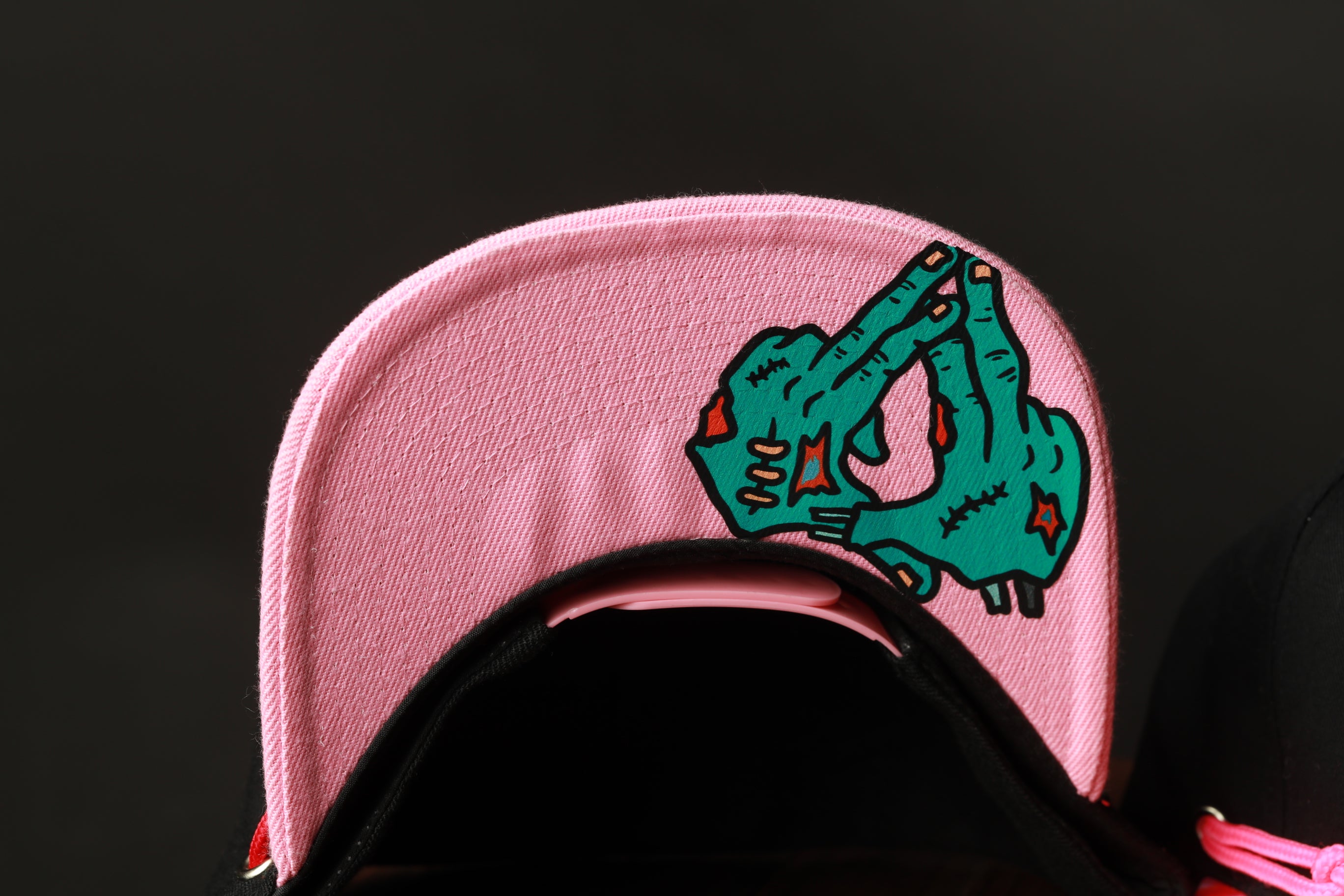 A close-up view of a pink baseball cap with a graphic of a green zombie hand on it.
