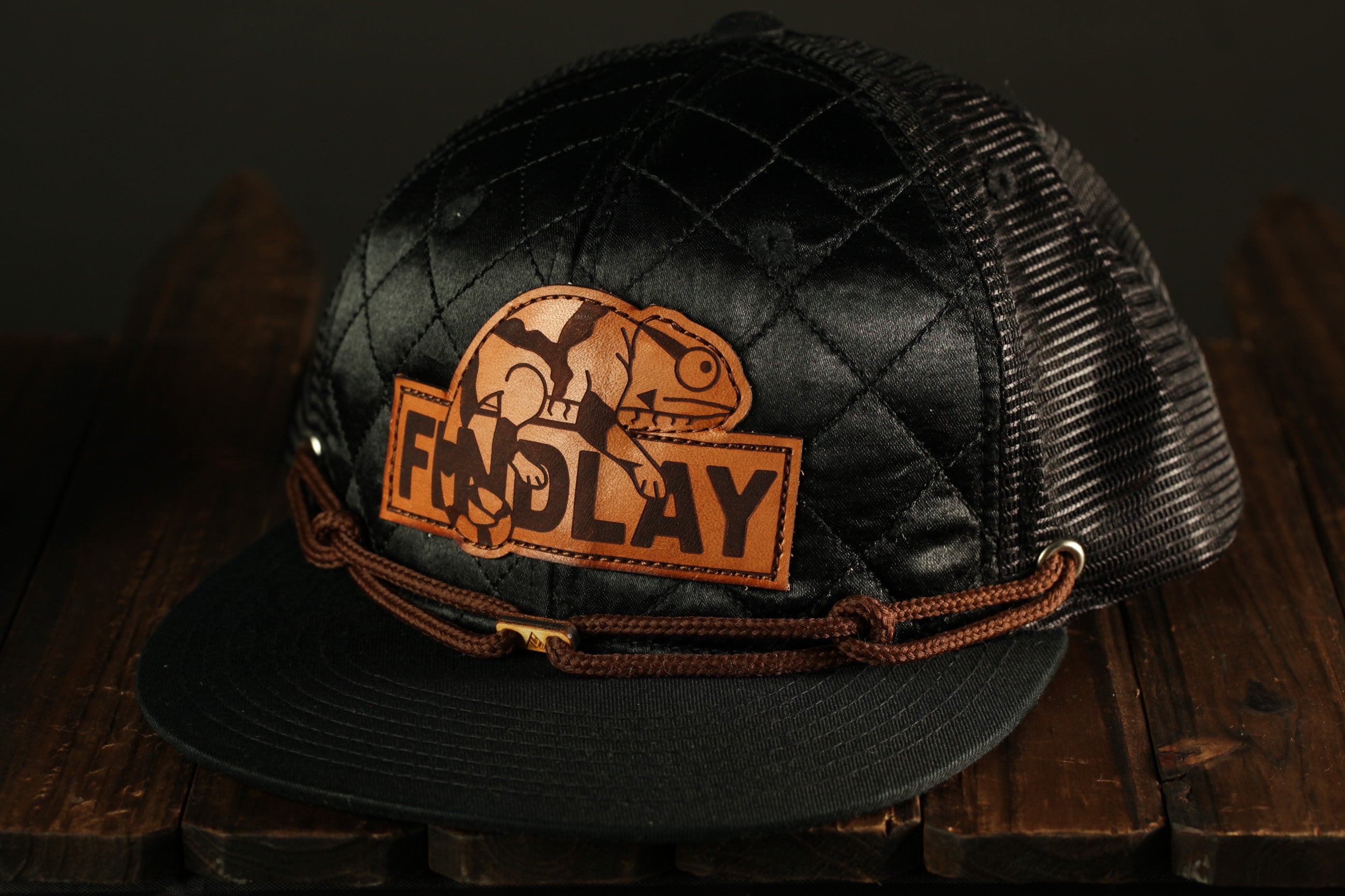 A black baseball cap with a quilted pattern and a patch featuring a chameleon.