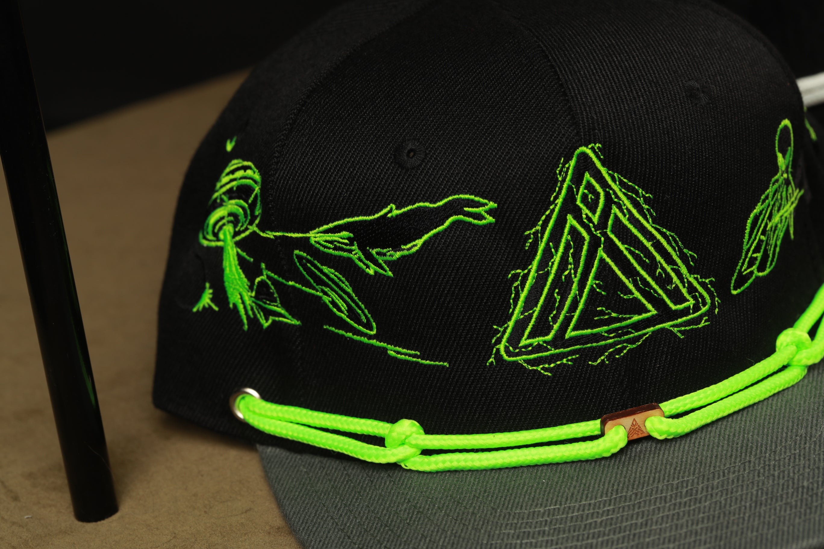A black baseball cap with green embroidered designs, including a triangle and a fish, is shown in the image.