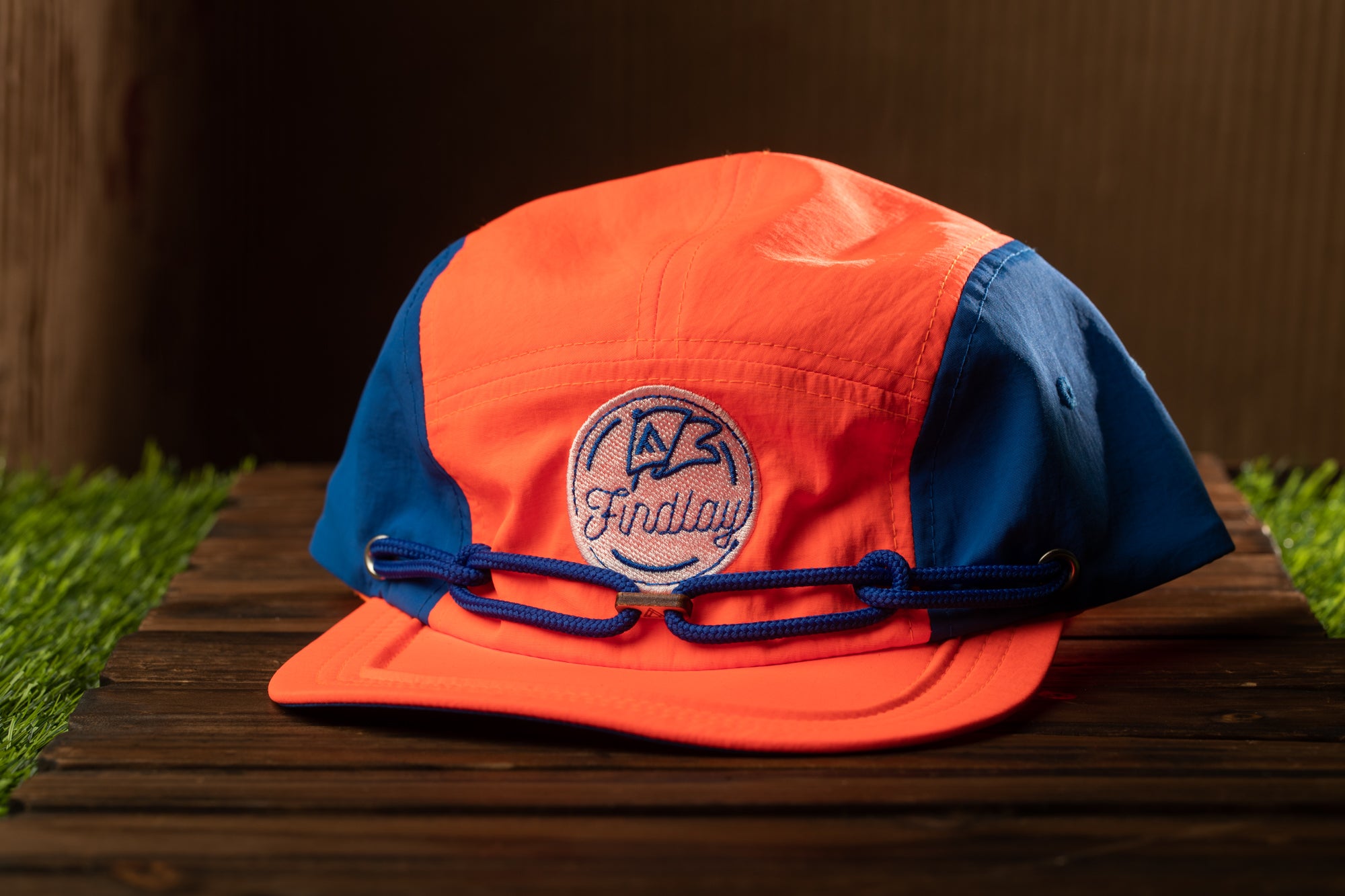 An orange and blue baseball cap with a blue logo on the front, placed on a wooden surface.