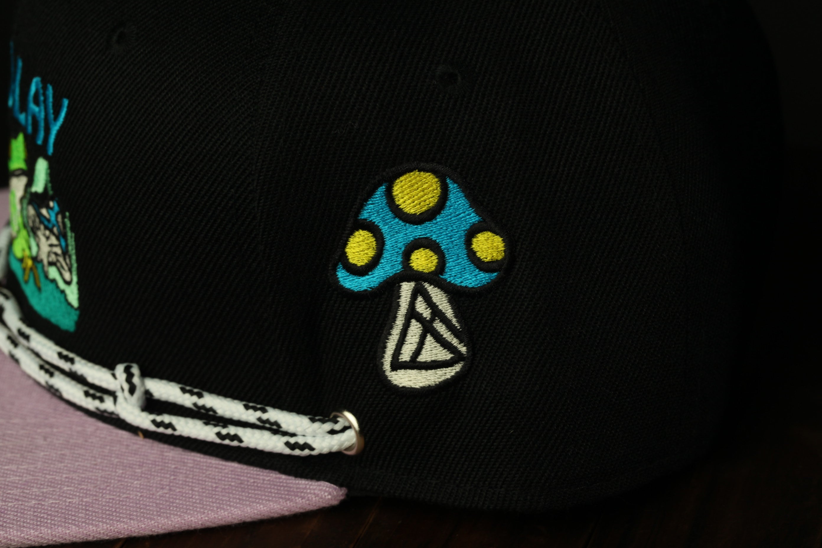 a close-up view of a black baseball cap with a colorful mushroom embroidered on it.