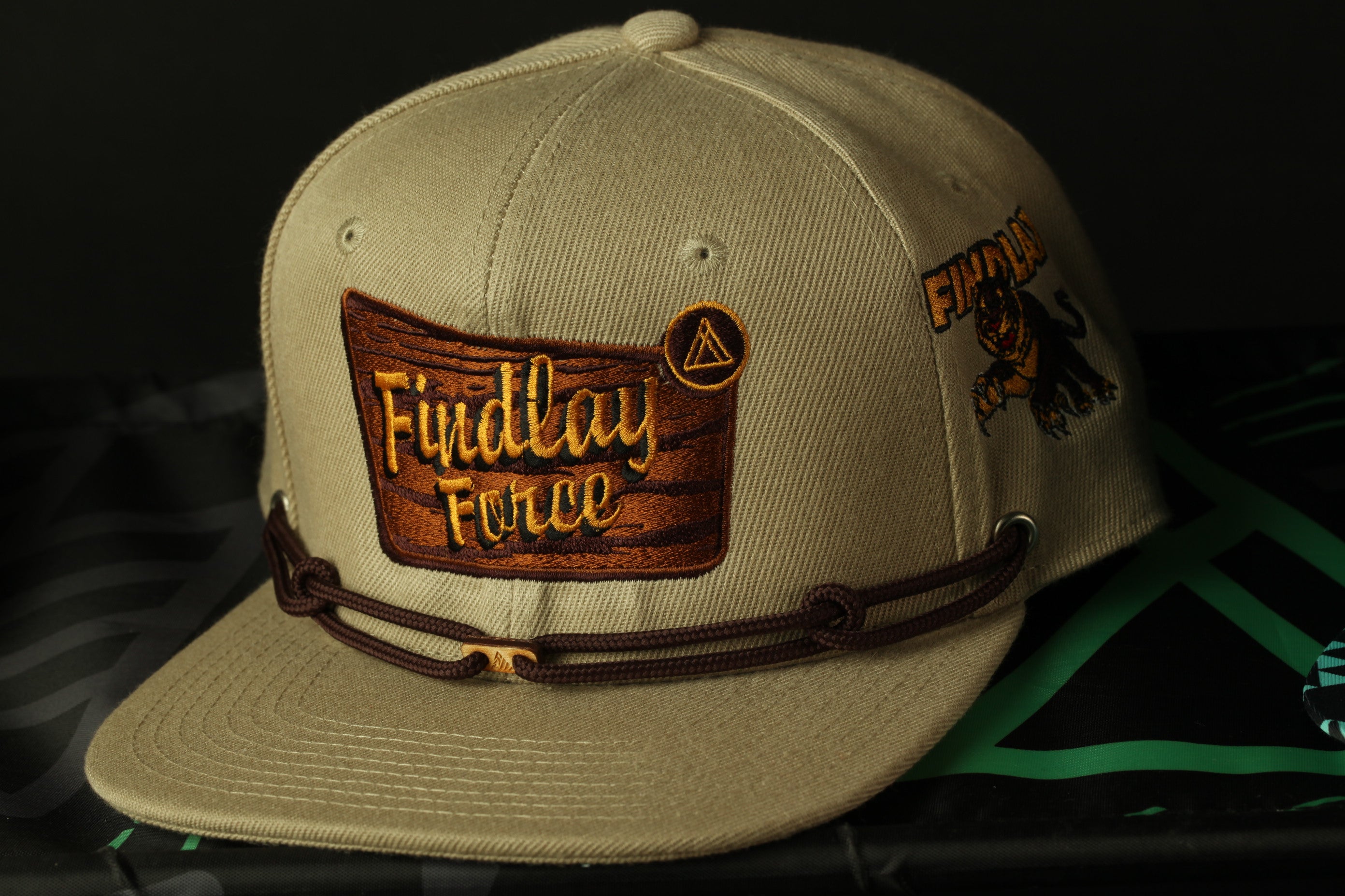 A tan baseball cap with a brown leather strap and a patch on the front, featuring the text "Fidday Force" and a graphic of a panther.