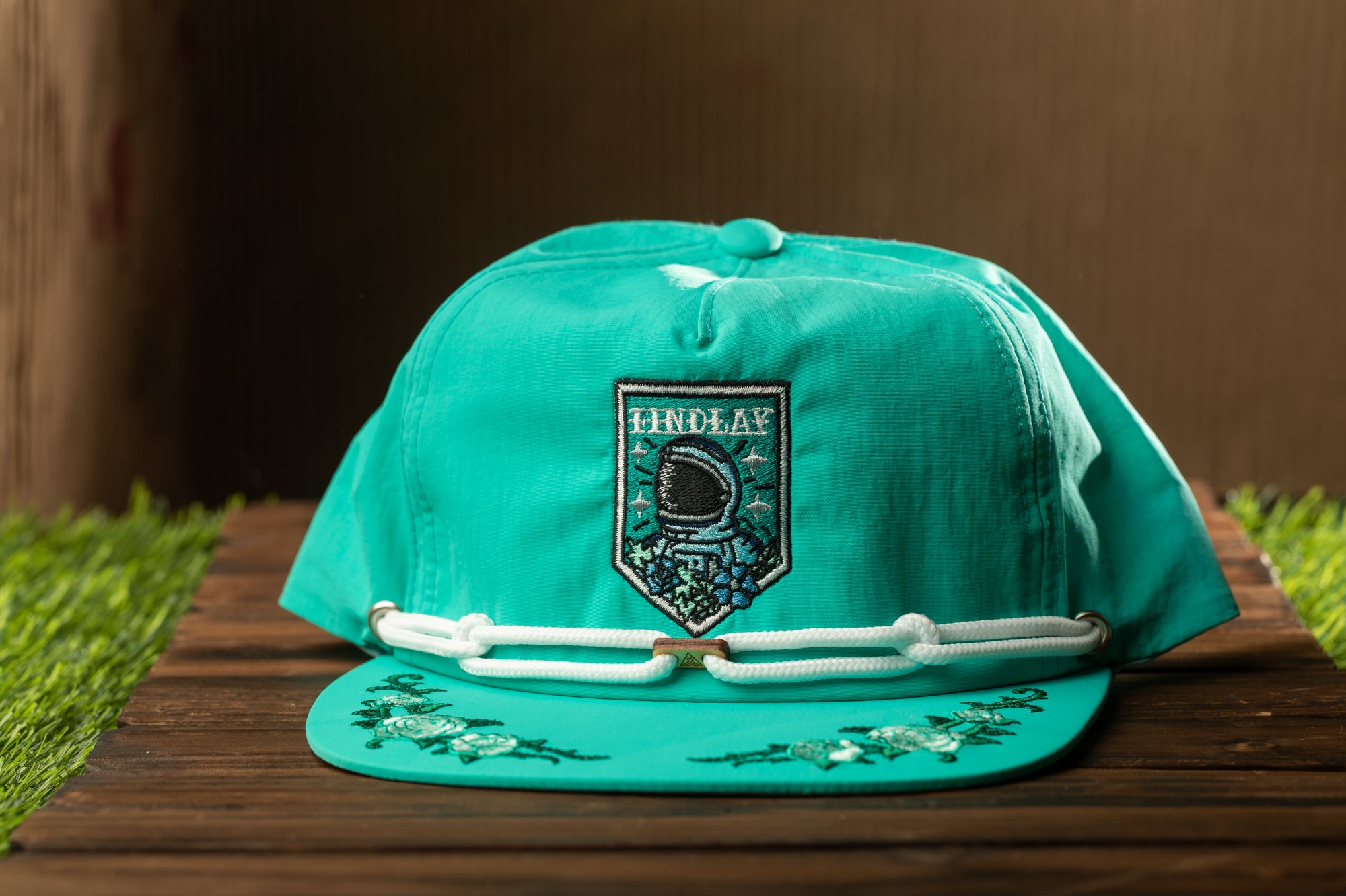 A turquoise baseball cap with a white rope and floral embroidery, featuring a patch with the word "EINPLAY" on it.