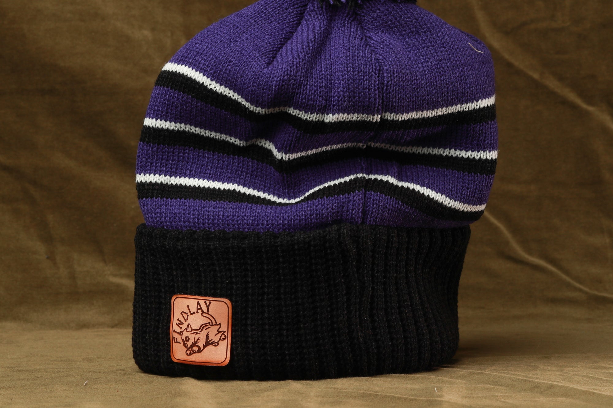 A purple and black striped beanie with a small orange patch on the front.