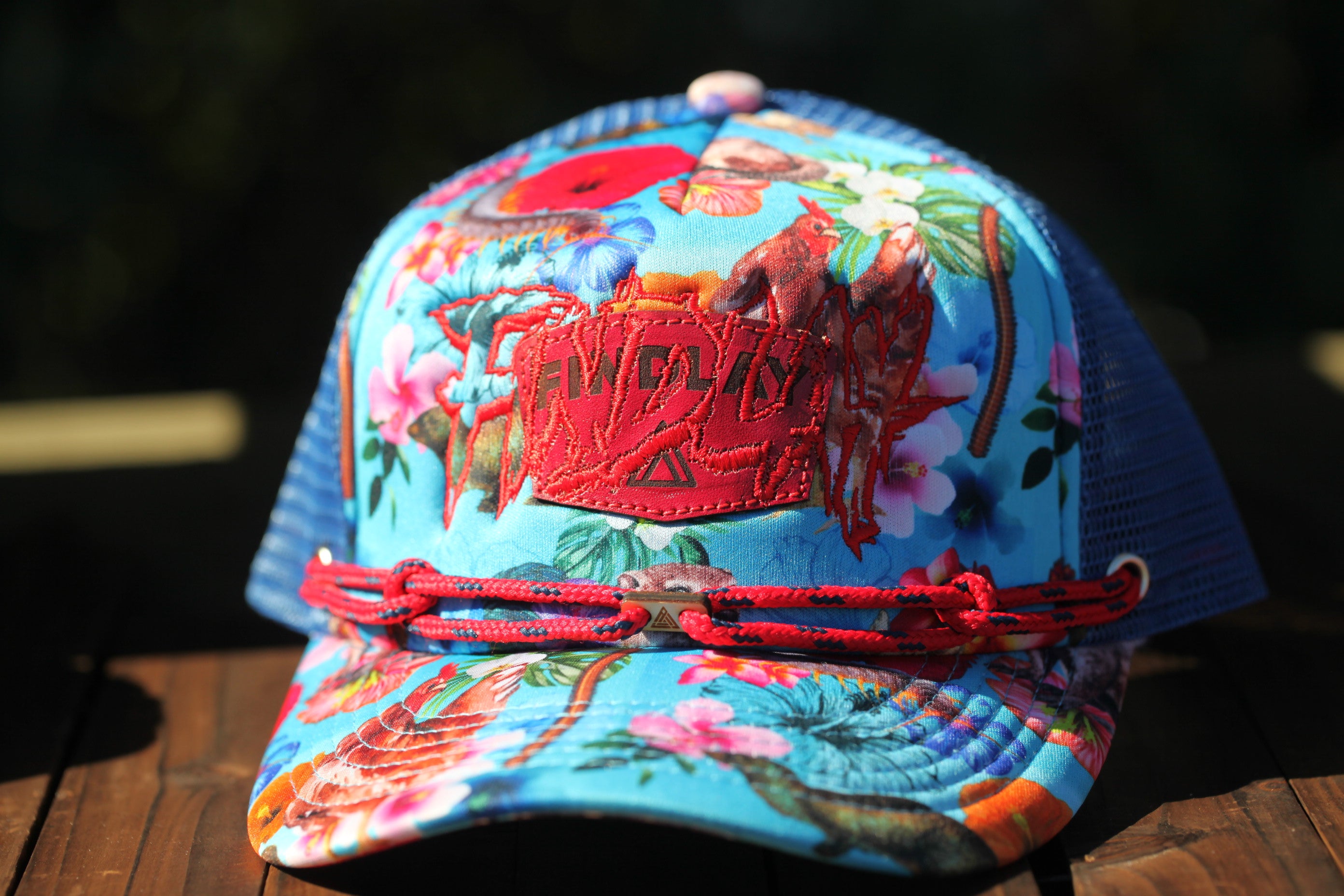 A colorful floral-patterned baseball cap with a red logo on the front, sitting on a wooden surface.