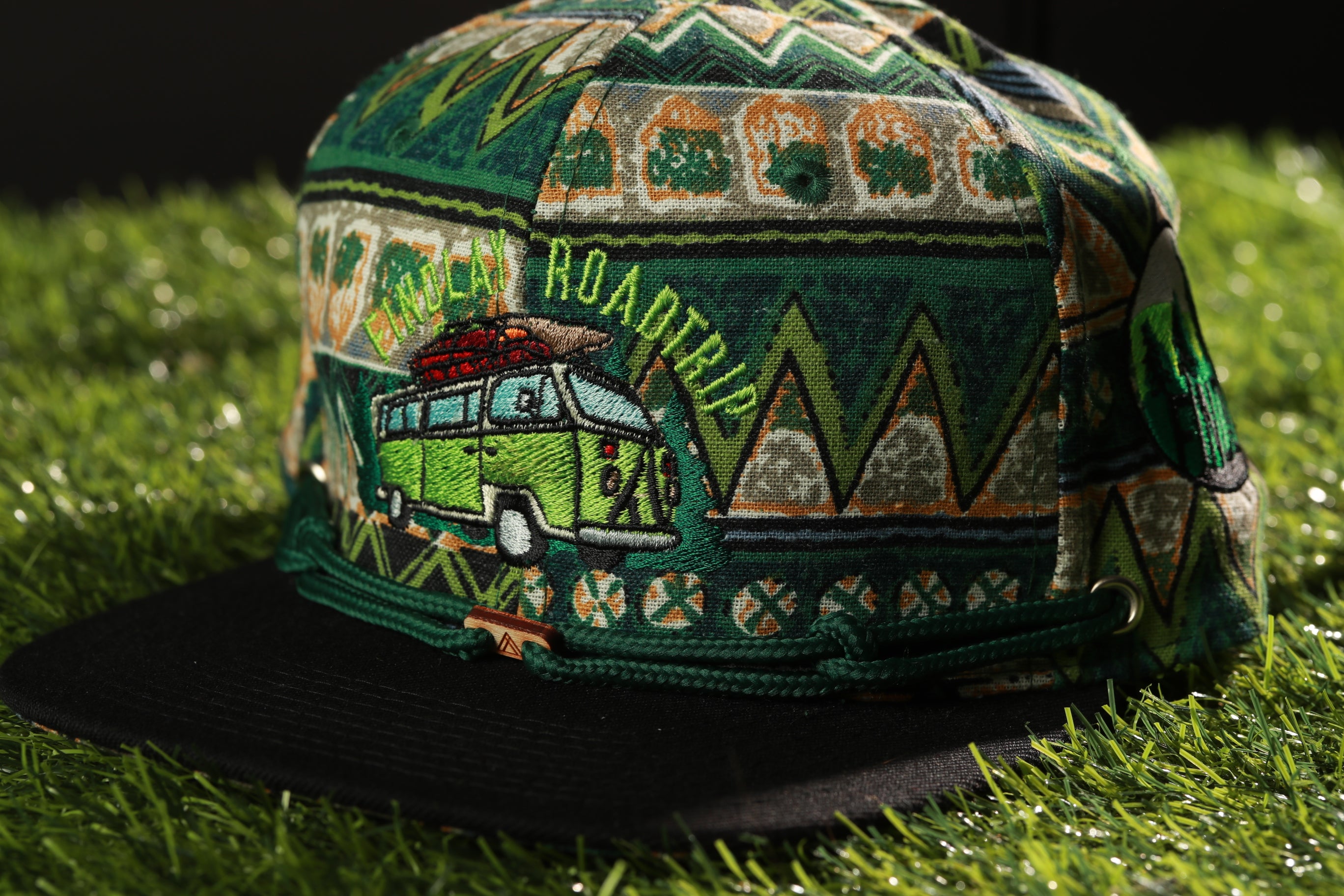 A colorful, patterned baseball cap with a green and orange design, featuring a cartoon van and the word "ROADTRIP" on the front.