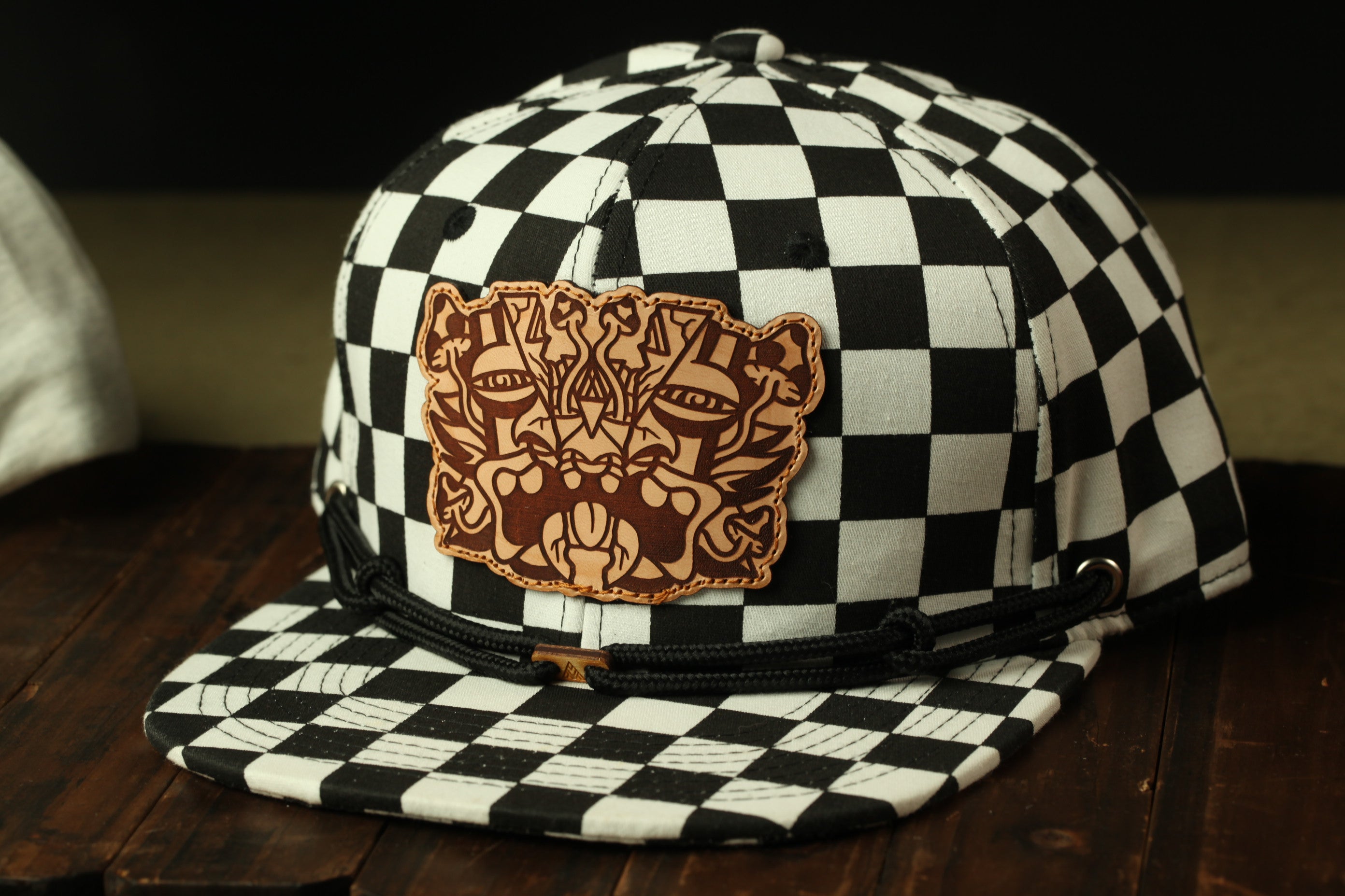 A black and white checkered baseball cap with a leather patch featuring an abstract design on the front.