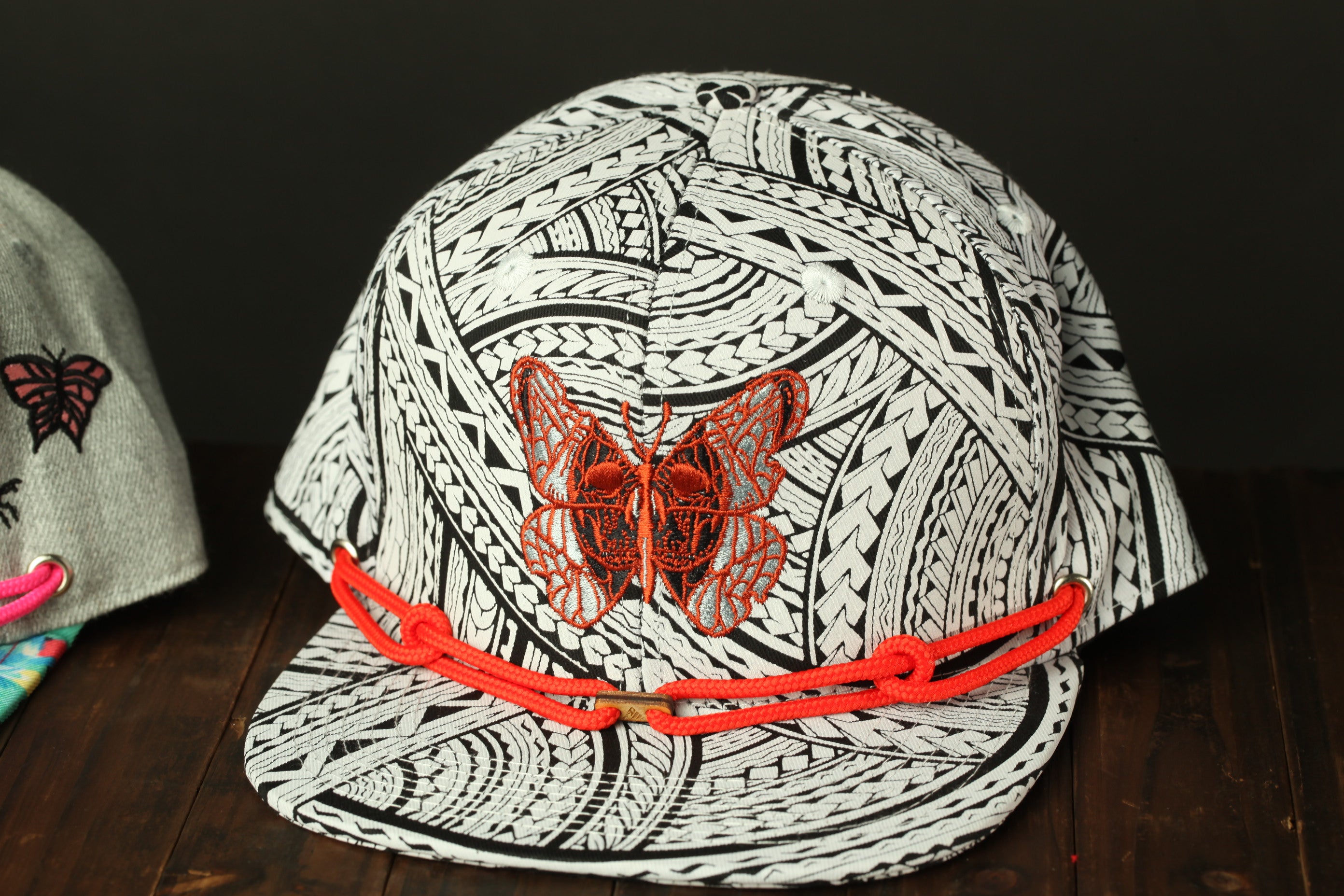 A black and white patterned baseball cap with a red butterfly embroidered on it, sitting on a wooden surface.