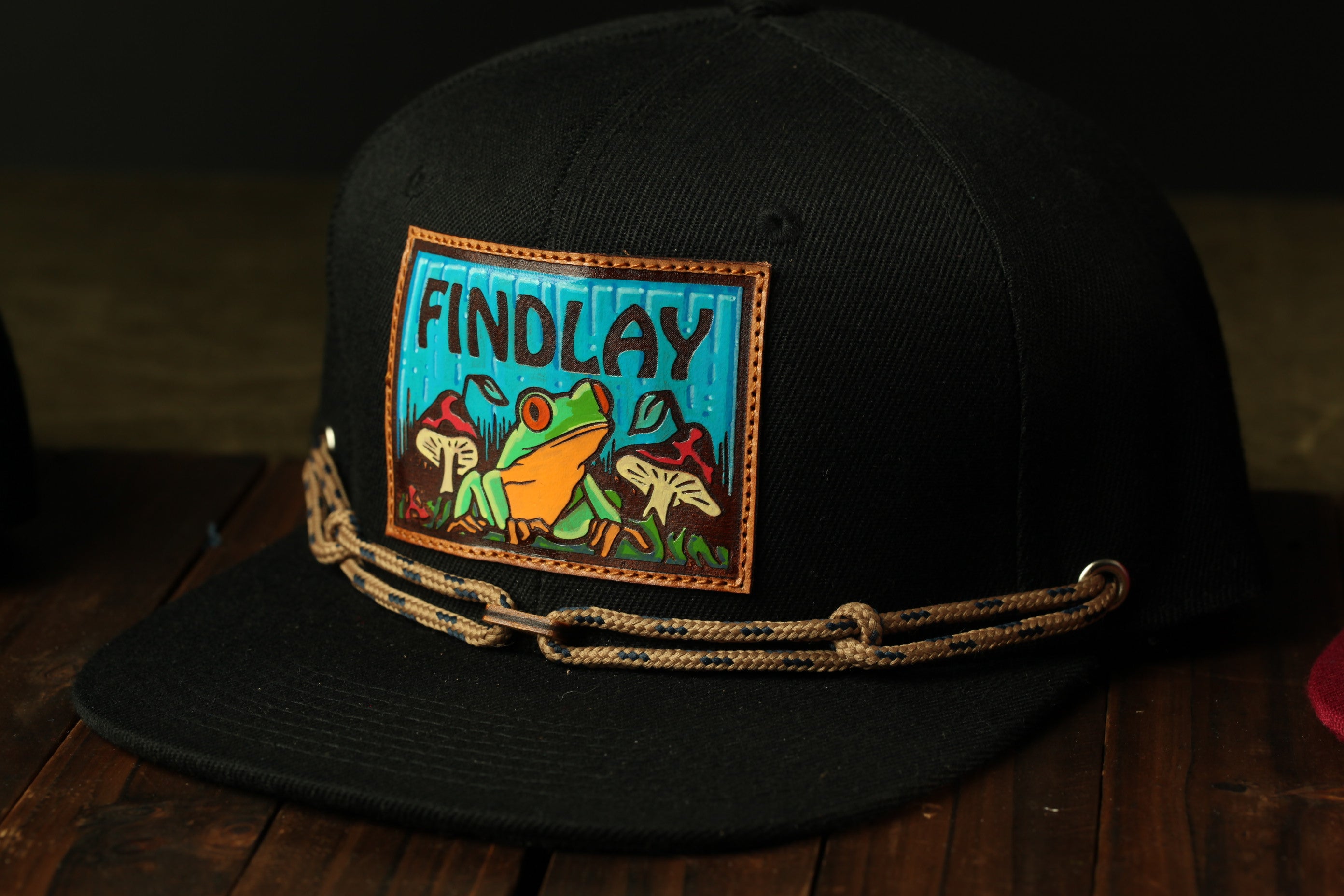 A black baseball cap with a colorful patch featuring a frog and mushrooms.
