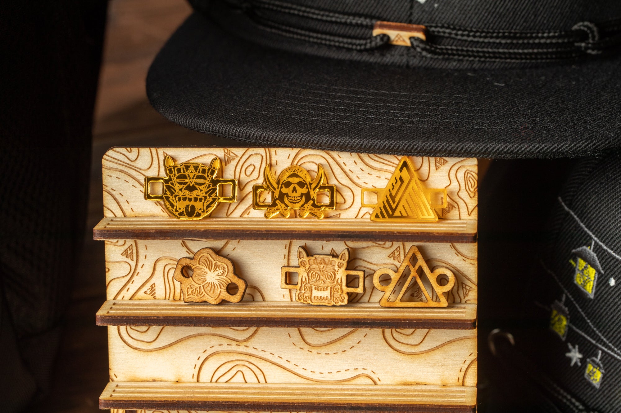 a wooden display case with various engraved objects, including a skull and crossbones, a triangle, and a bear. The display case is placed next to a black hat.