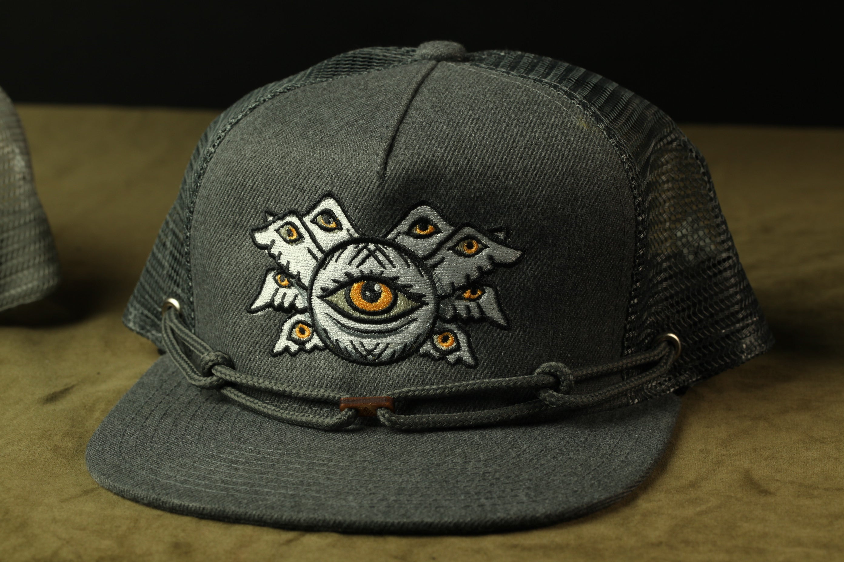 A gray baseball cap with an embroidered design on the front, featuring a large eye surrounded by smaller eyes.