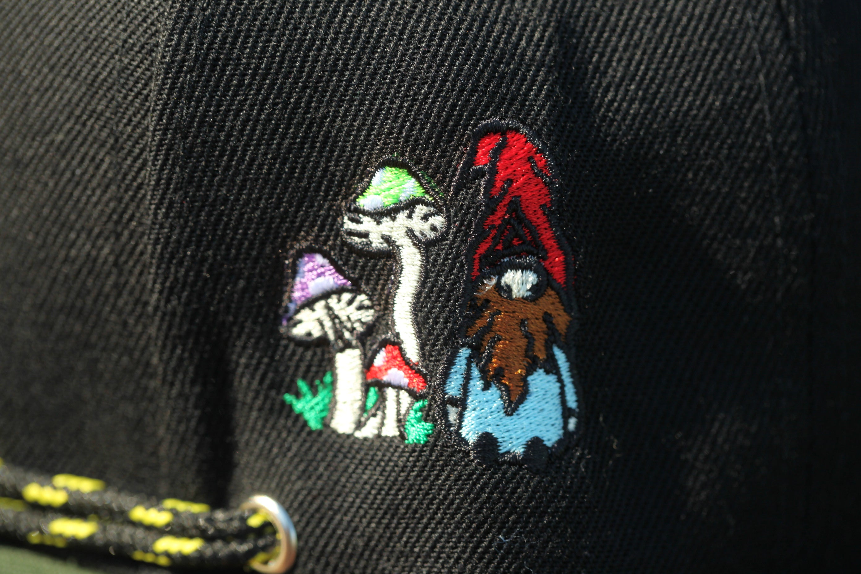 a close-up of a black fabric with a colorful, whimsical embroidered design depicting a gnome and mushrooms.