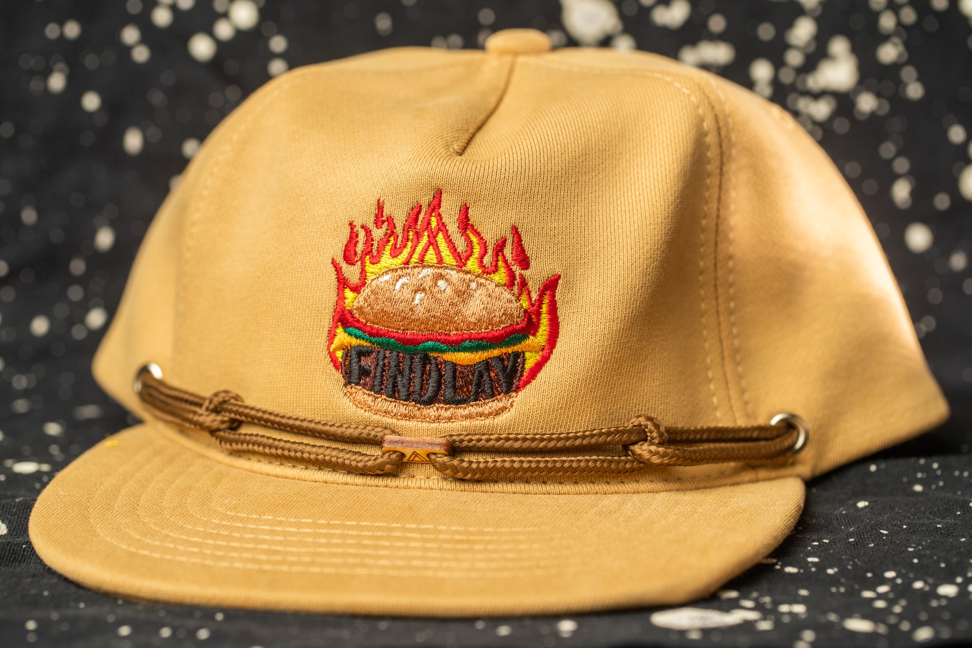 A beige baseball cap with a flame design on the front, featuring the text "FINDOLA" on the front.