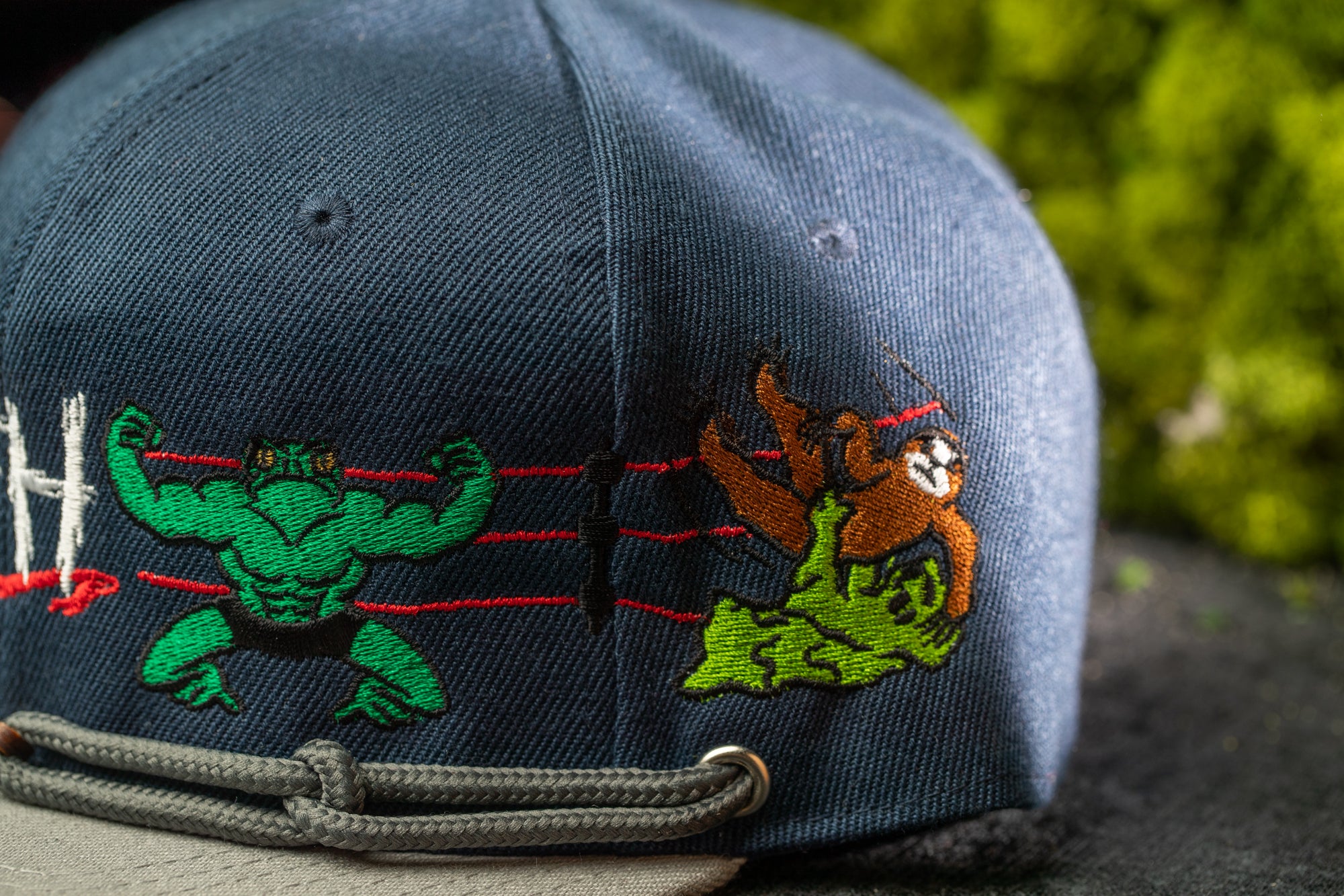 A close-up view of a dark blue baseball cap with colorful cartoon-style characters on it, including a muscular green character and a brown character.