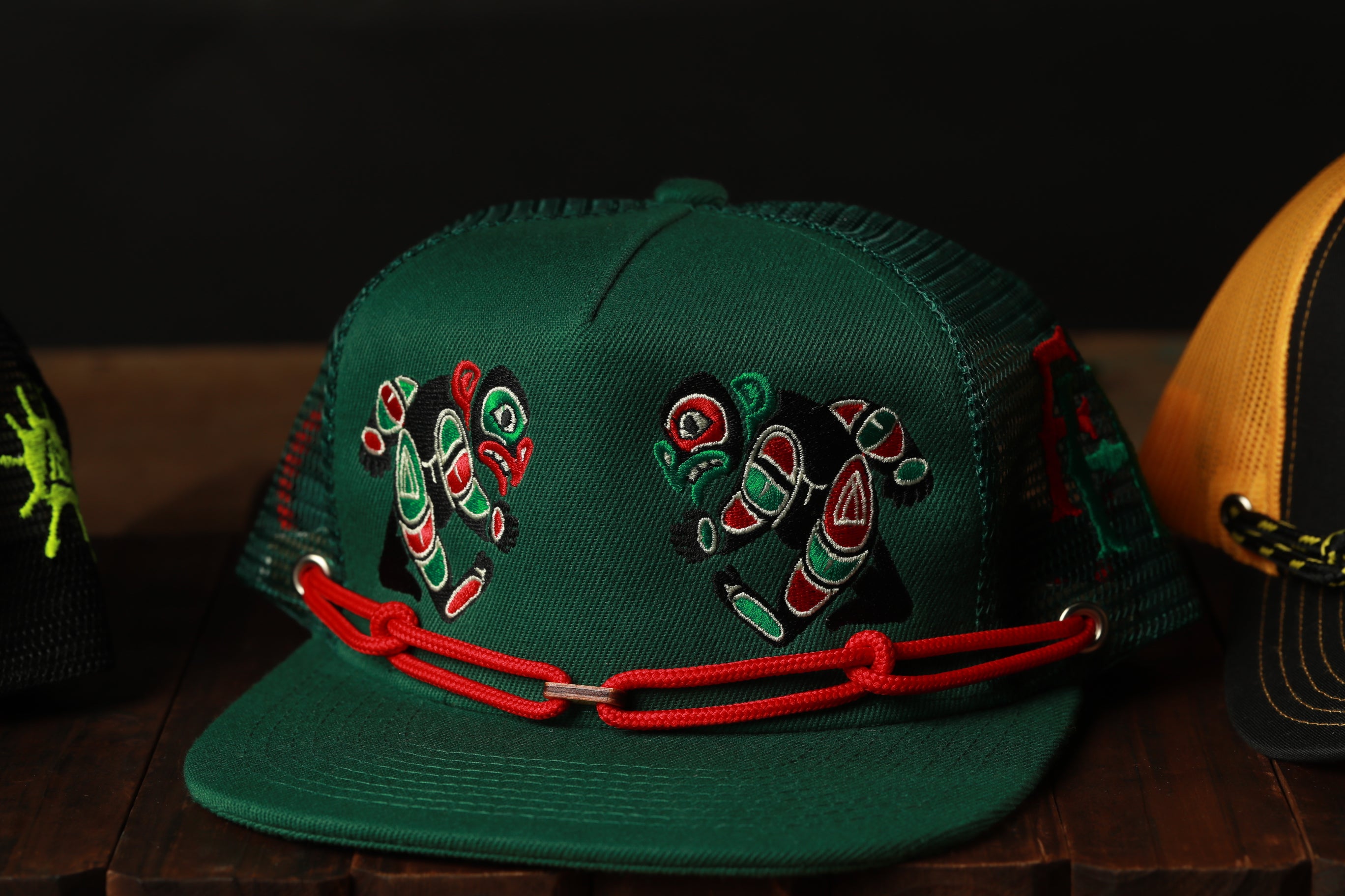 A green baseball cap with red and green embroidered designs on the front, sitting on a wooden surface.