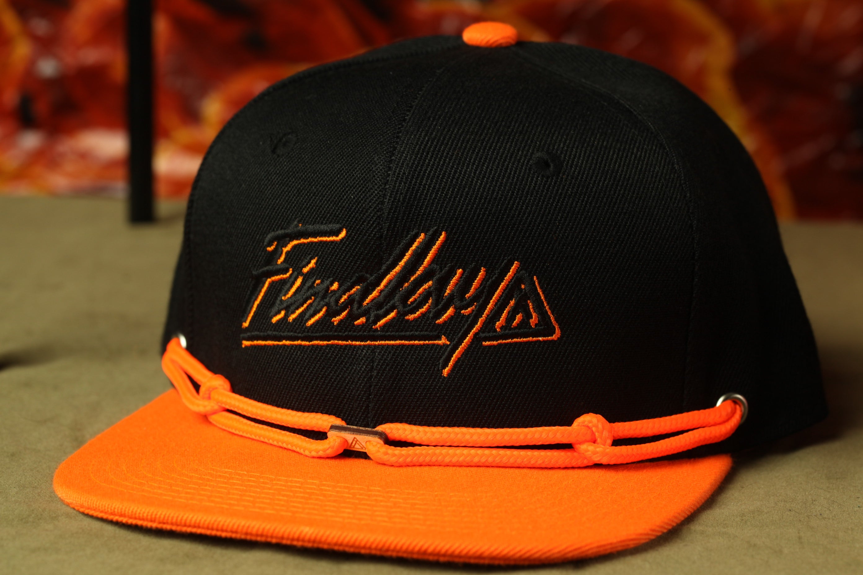 A black baseball cap with an orange brim and a black logo on the front.