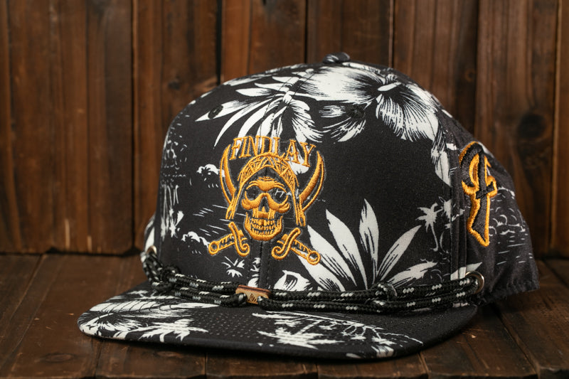 A black and white floral baseball cap with a skull and crossbones design, placed on a wooden surface.