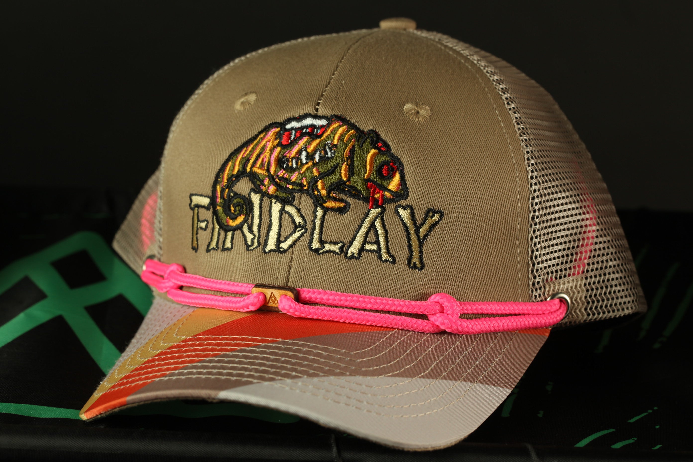 A tan baseball cap with a colorful design and a pink string around the brim.