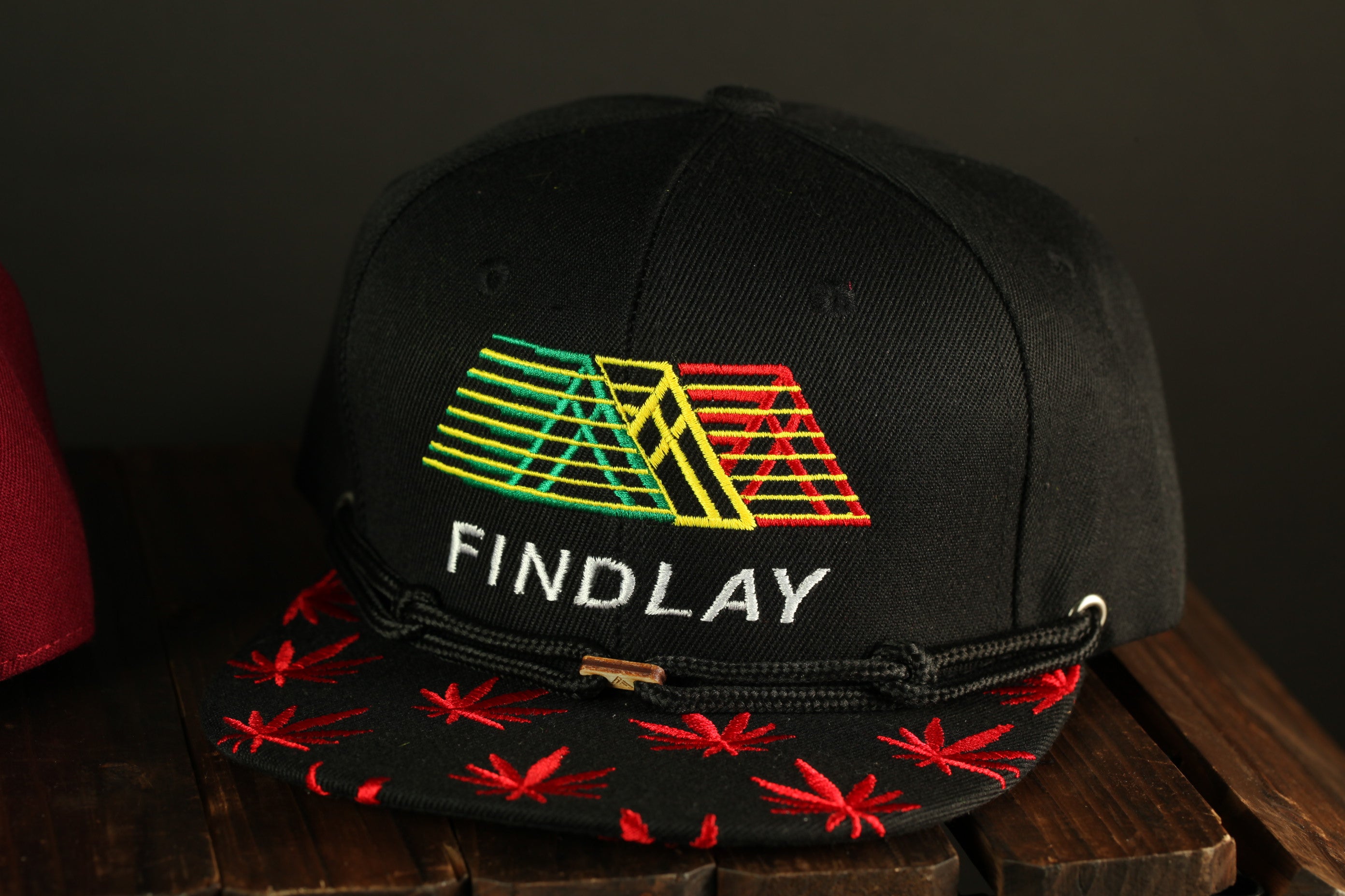 A black baseball cap with a colorful geometric design and the word "FINDLAY" printed on it, sitting on a wooden surface.