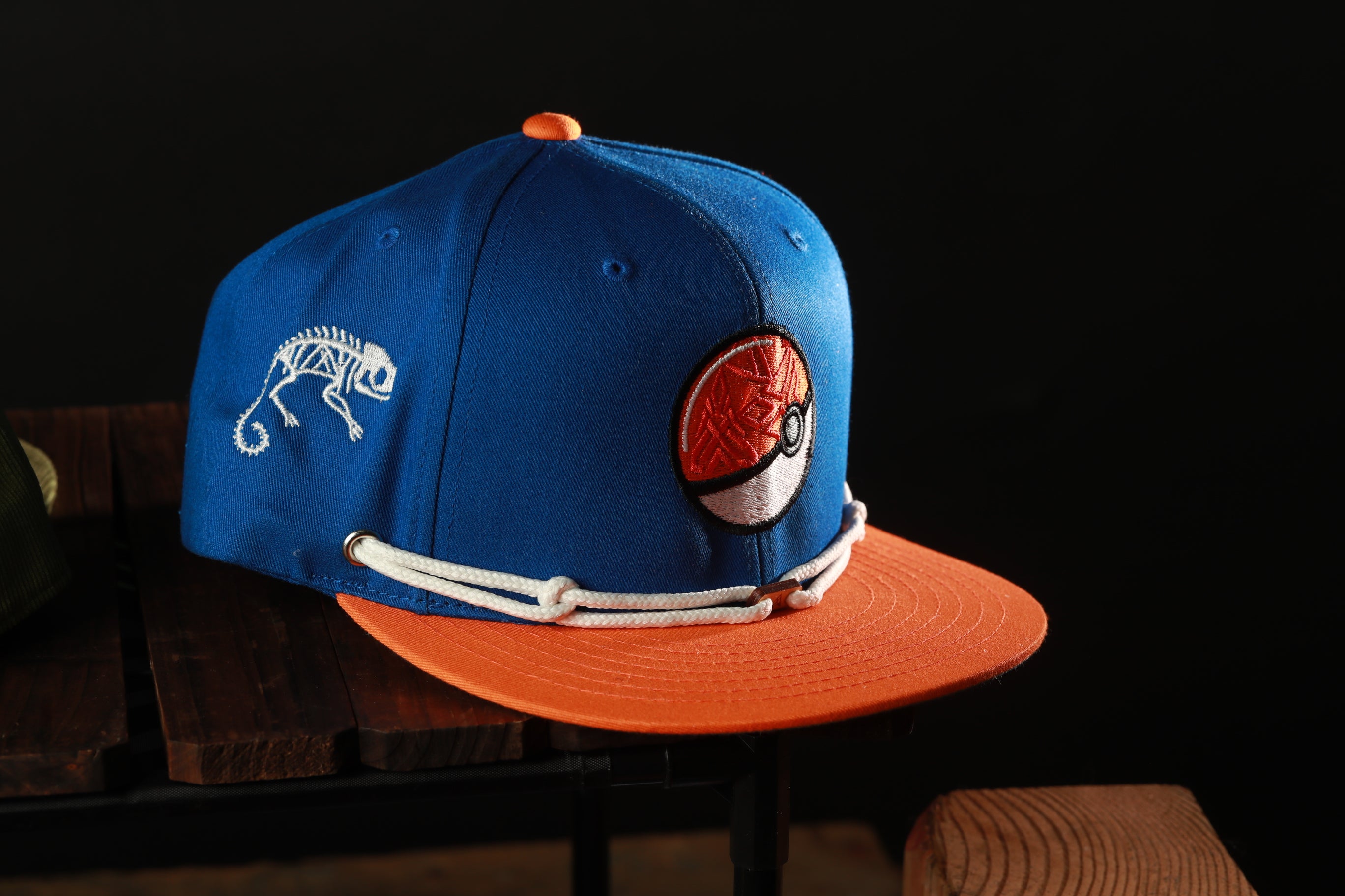 A blue baseball cap with an orange brim and a white logo on the front, sitting on a wooden surface.
