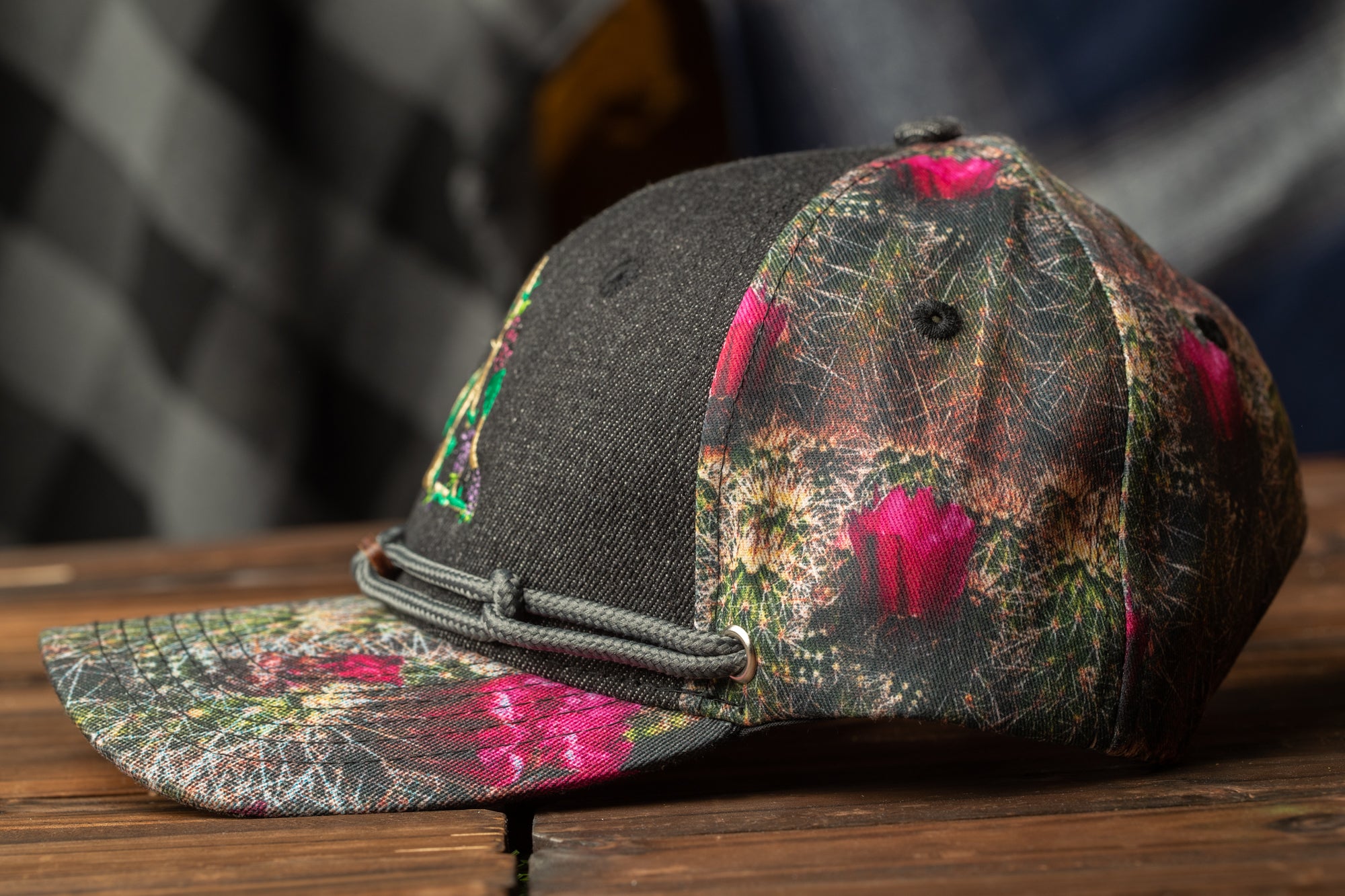 A black baseball cap with a colorful floral pattern on the front and brim, resting on a wooden surface.