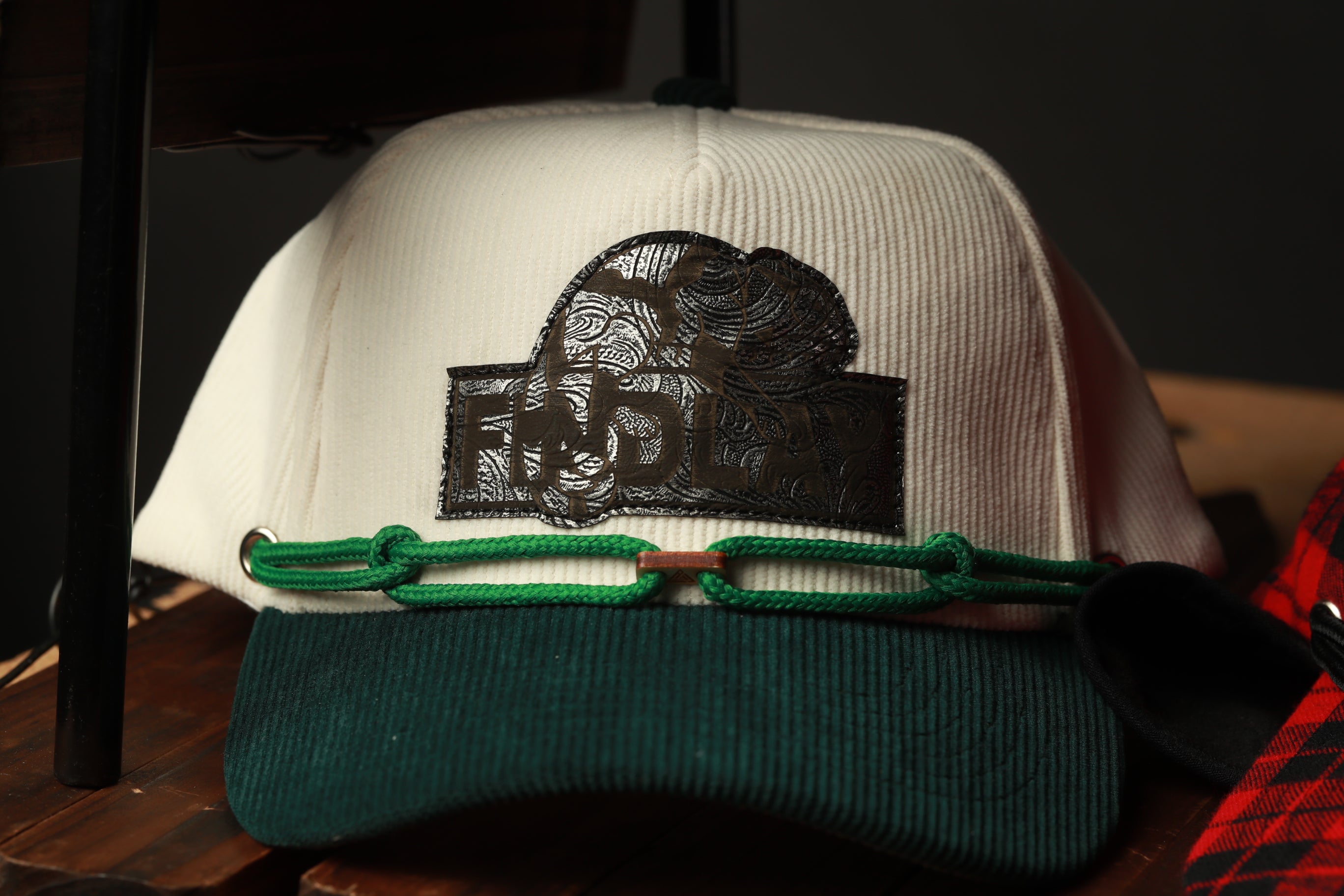 A white baseball cap with a green brim and a black logo on the front, sitting on a wooden surface.