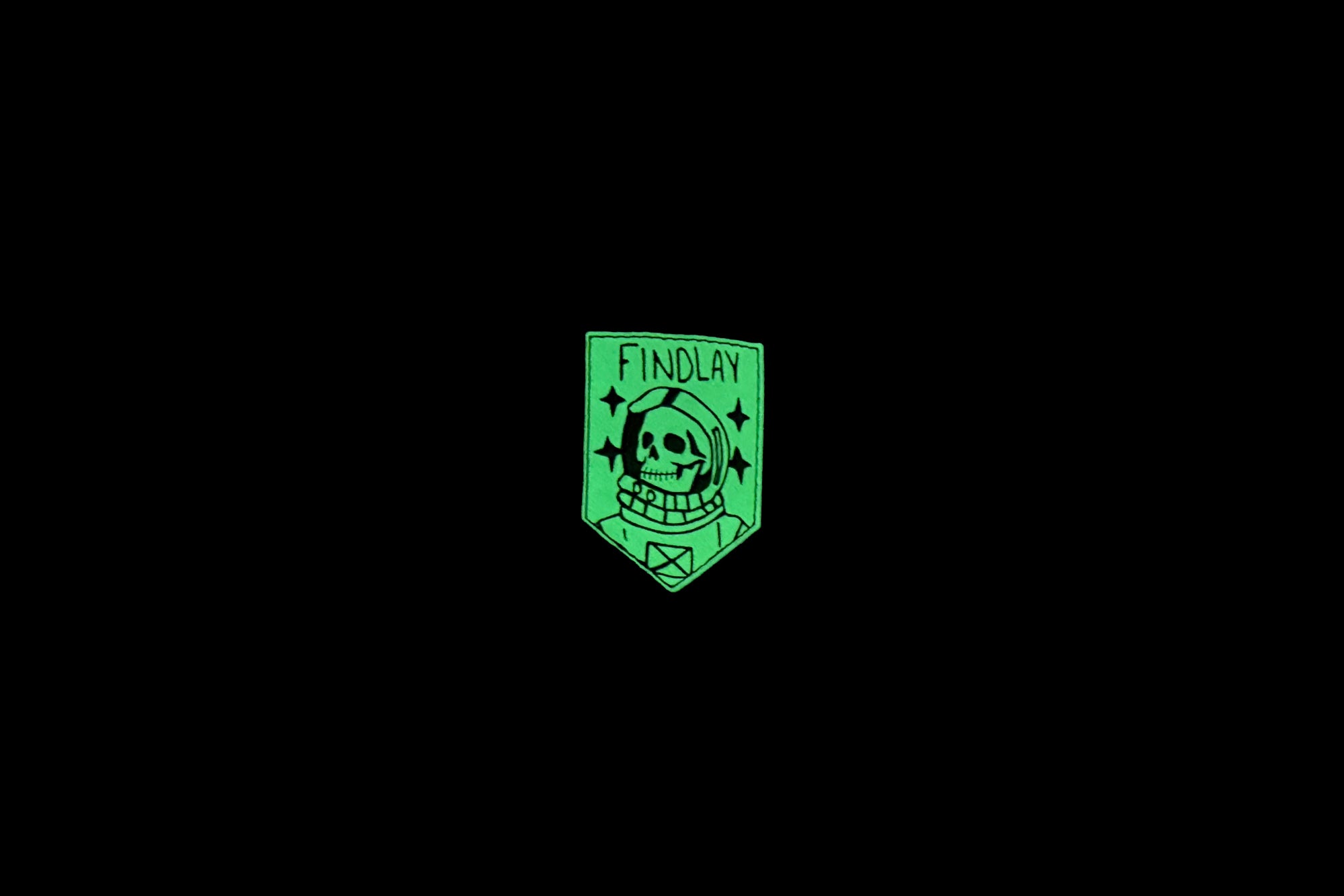 A green patch with a skull and crossbones design, surrounded by stars, against a black background.