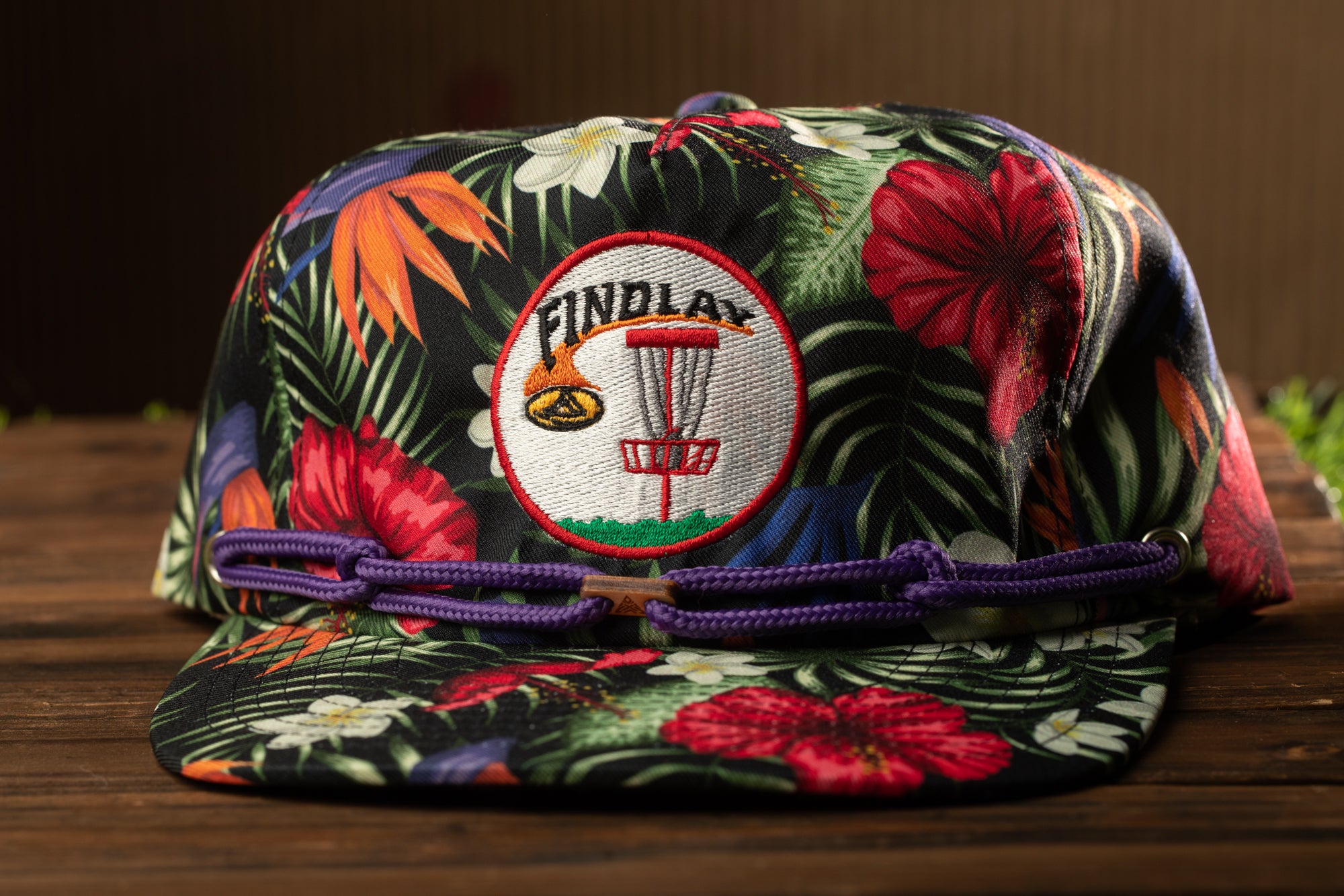 A colorful floral cap with a frisbee design and the word "FINDLAY" on it, placed on a wooden surface.