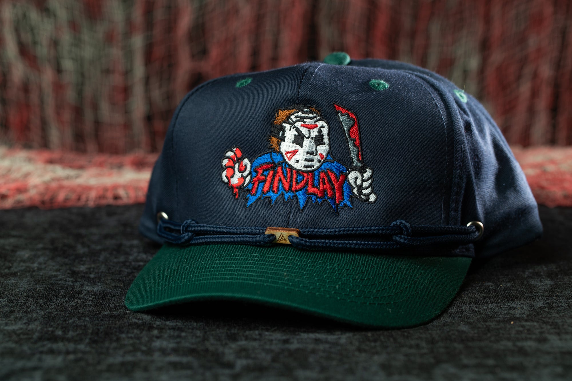 A dark blue baseball cap with a cartoon character design and the word "FINDPLAY" printed on it.